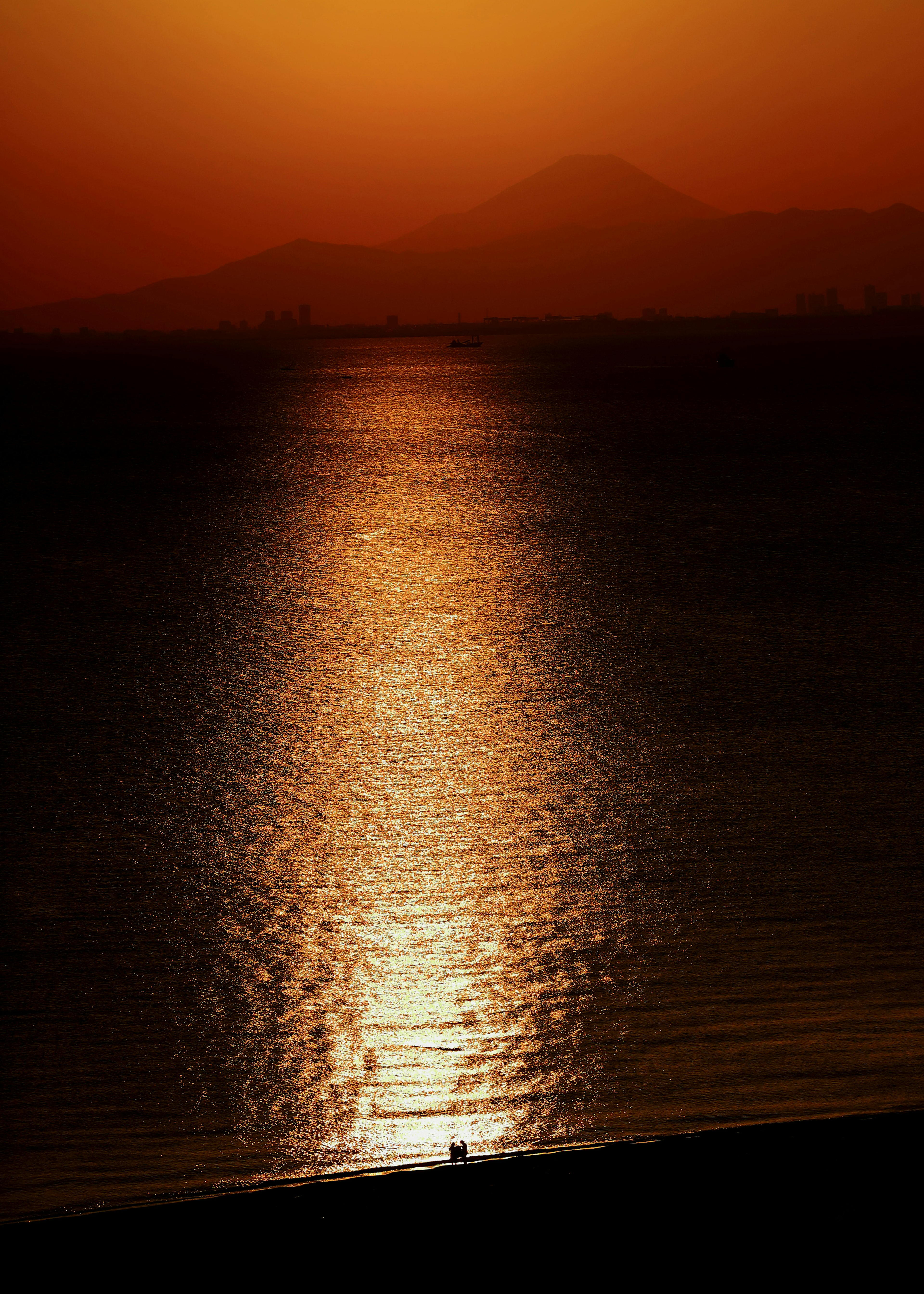 夕焼けの海の反射とシルエットの山