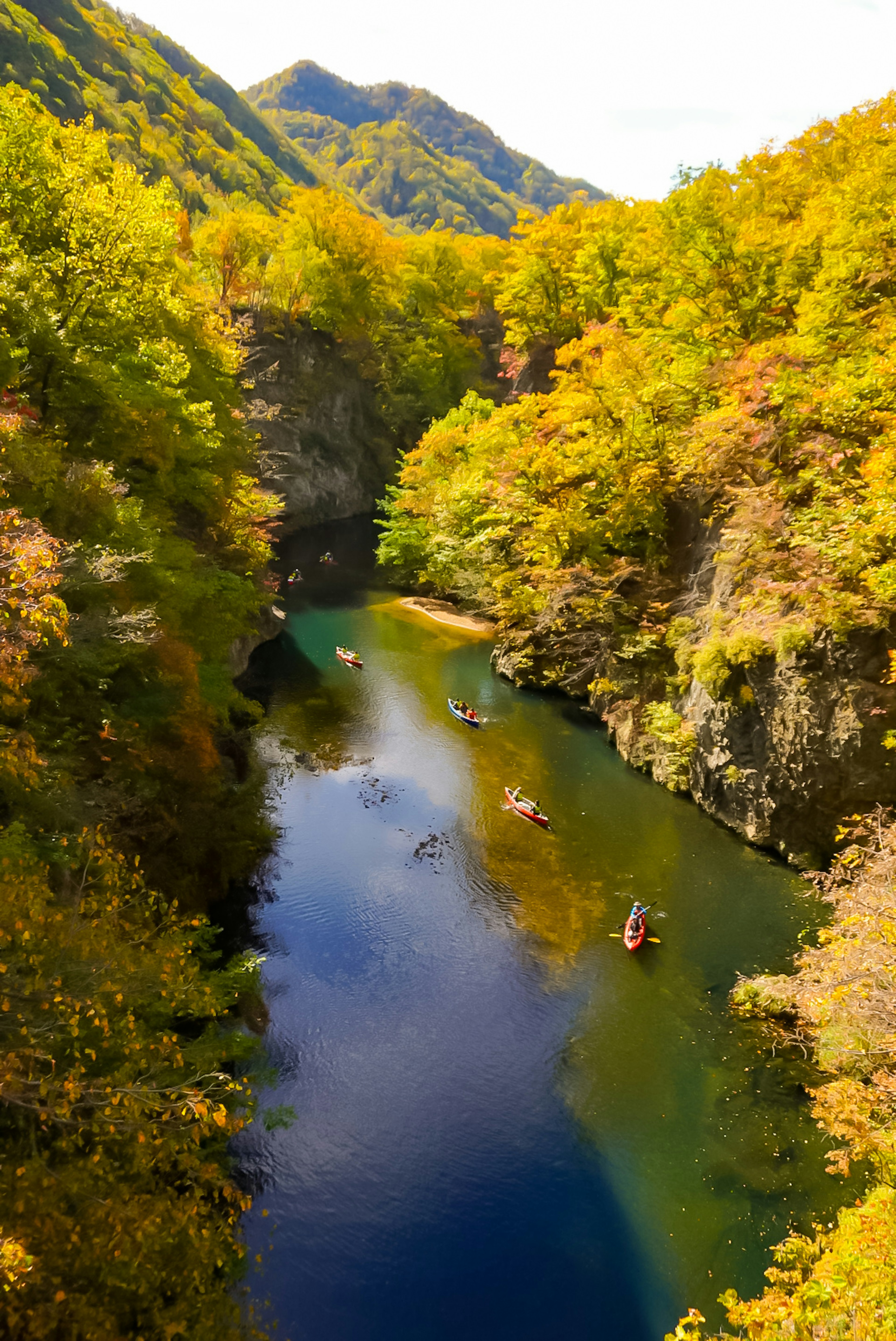 Schöne Herbstlandschaft mit Bergen, die mit gelben und orangefarbenen Blättern bedeckt sind, und einem ruhigen Fluss