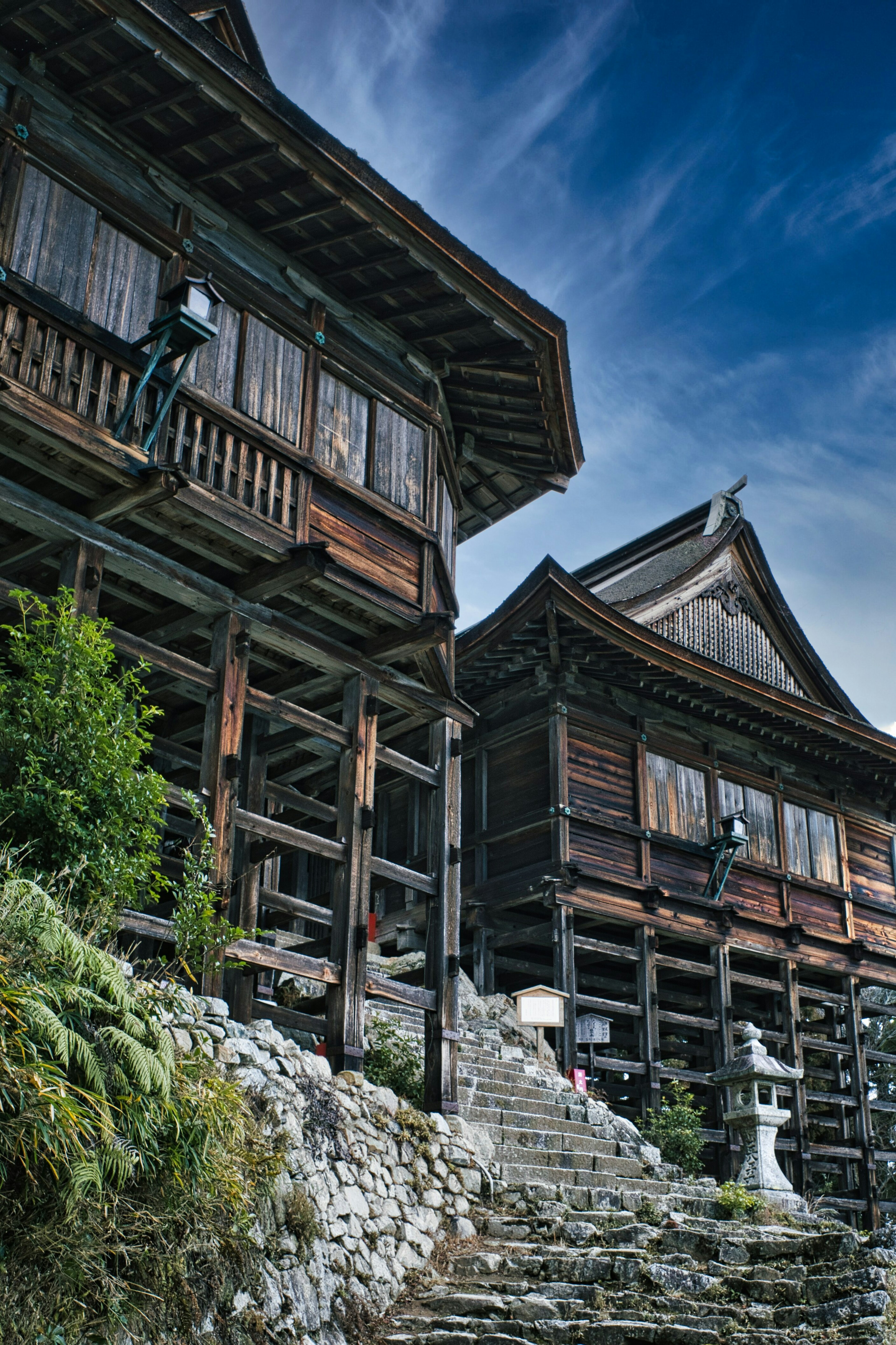 Deux bâtiments en bois traditionnels avec des escaliers en pierre et un ciel bleu