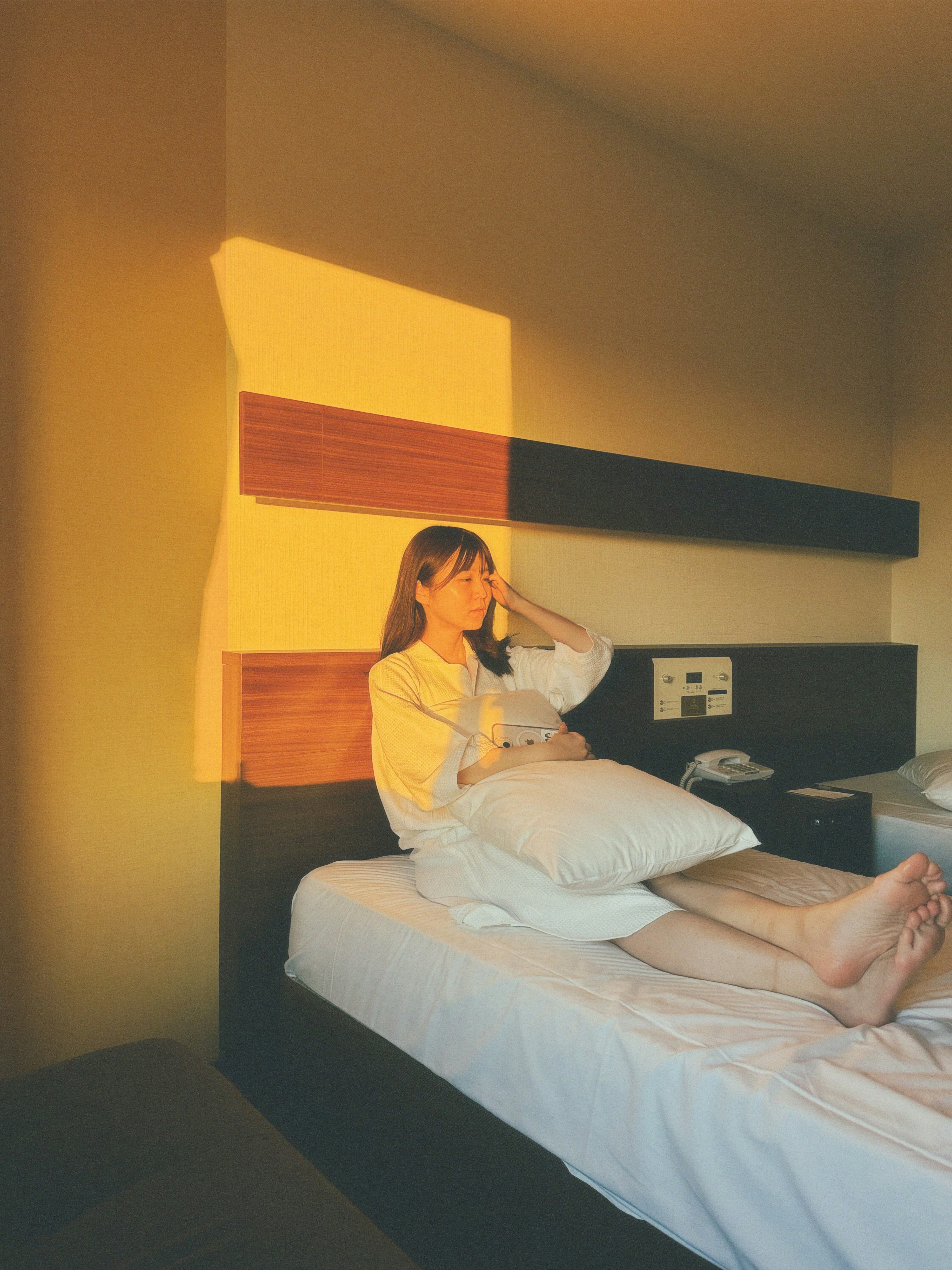 A woman sitting on a bed holding a white pillow in a sunlit room