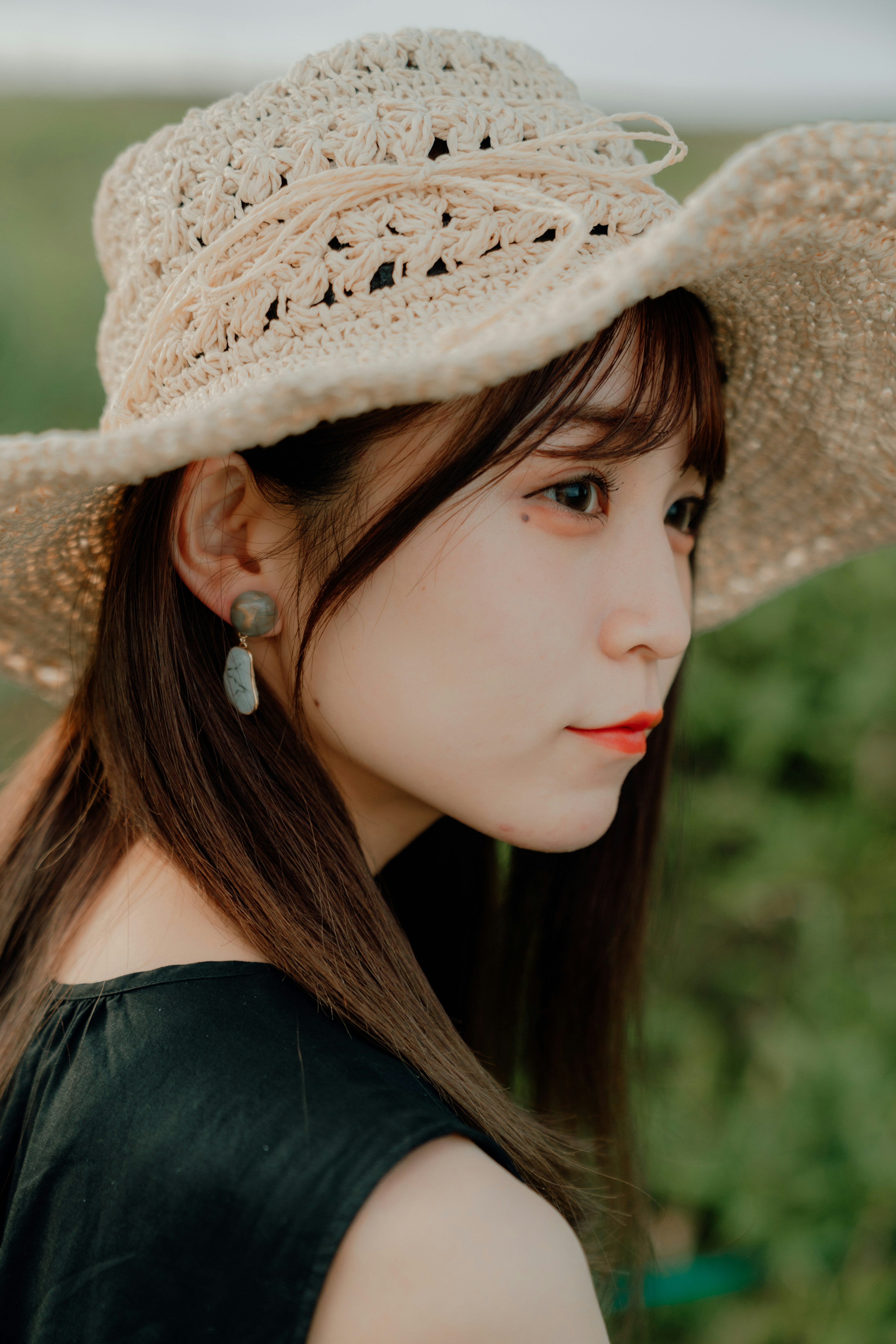 Side profile of a woman wearing a straw hat black top and large earrings