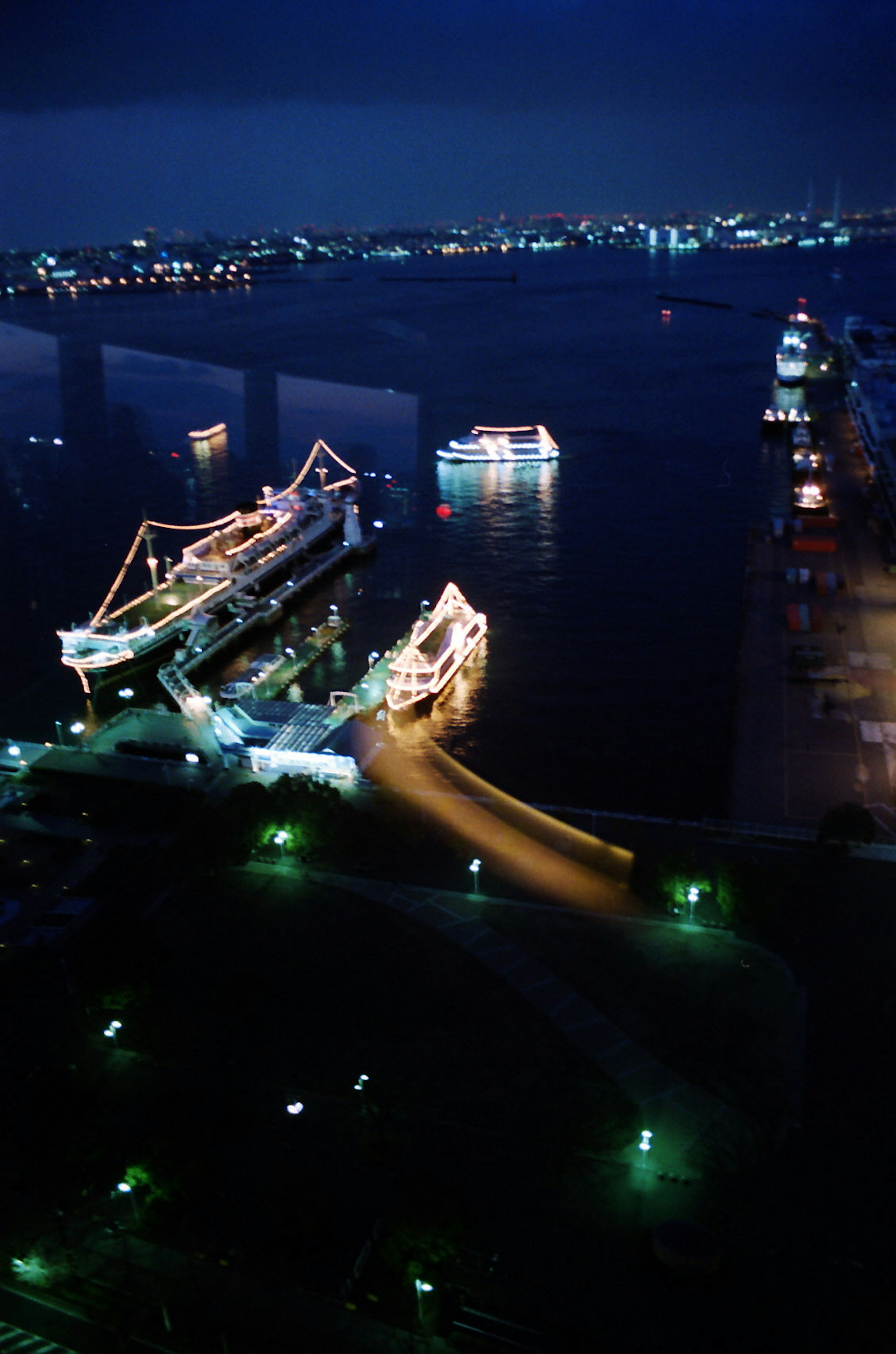 Vista nocturna de un puerto con barcos iluminados y muelle