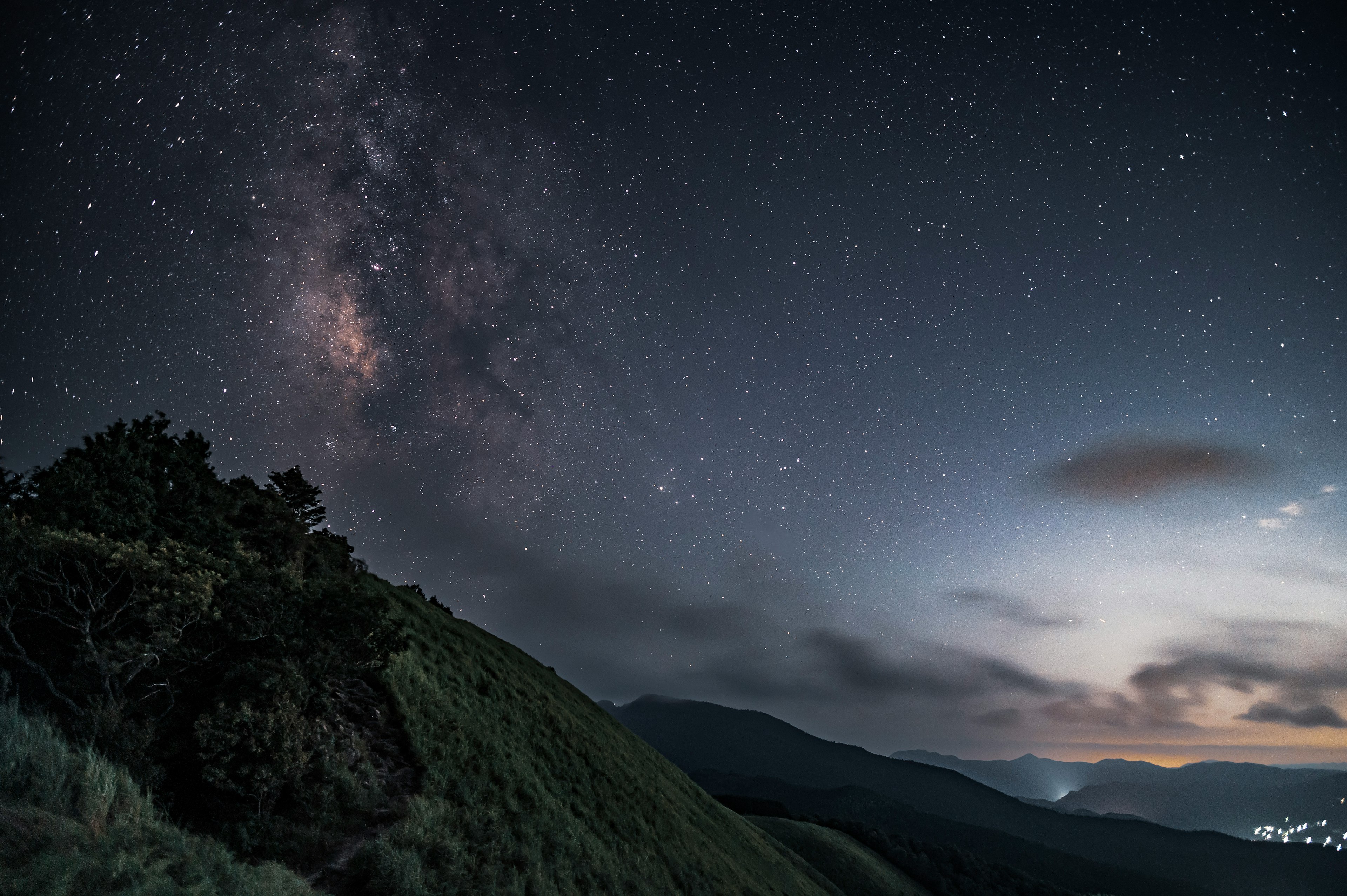 Night landscape featuring the starry sky and Milky Way visible over green hills and mountains