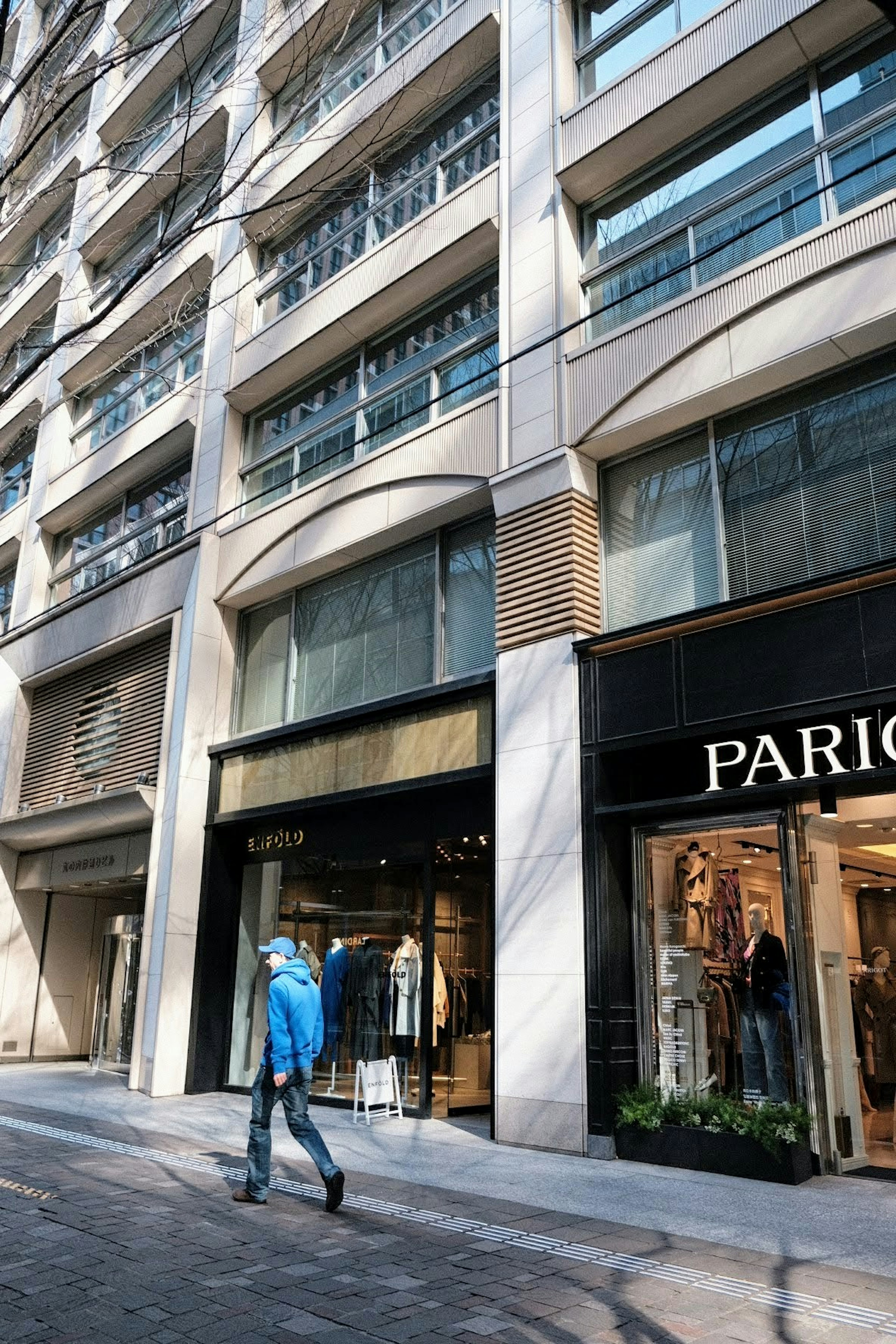 Eine Person in blauer Jacke, die vor einem Geschäft in Paris in einer Stadtlandschaft geht