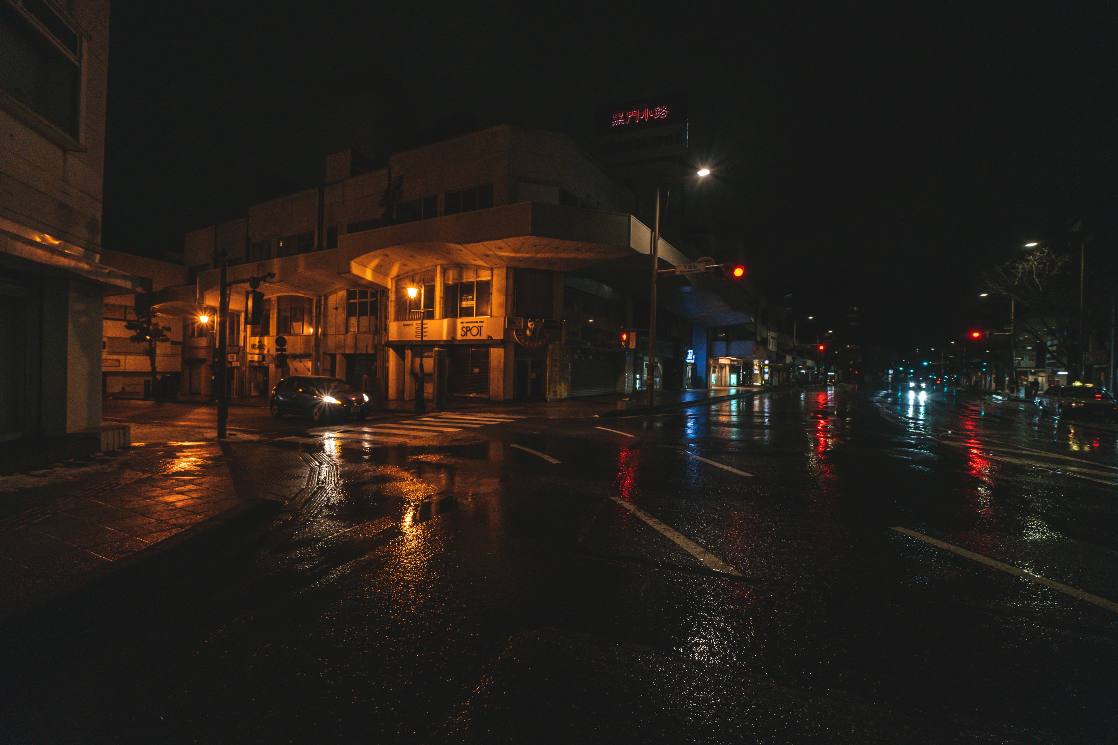 Quiet street corner at night with wet roads and orange streetlights reflecting