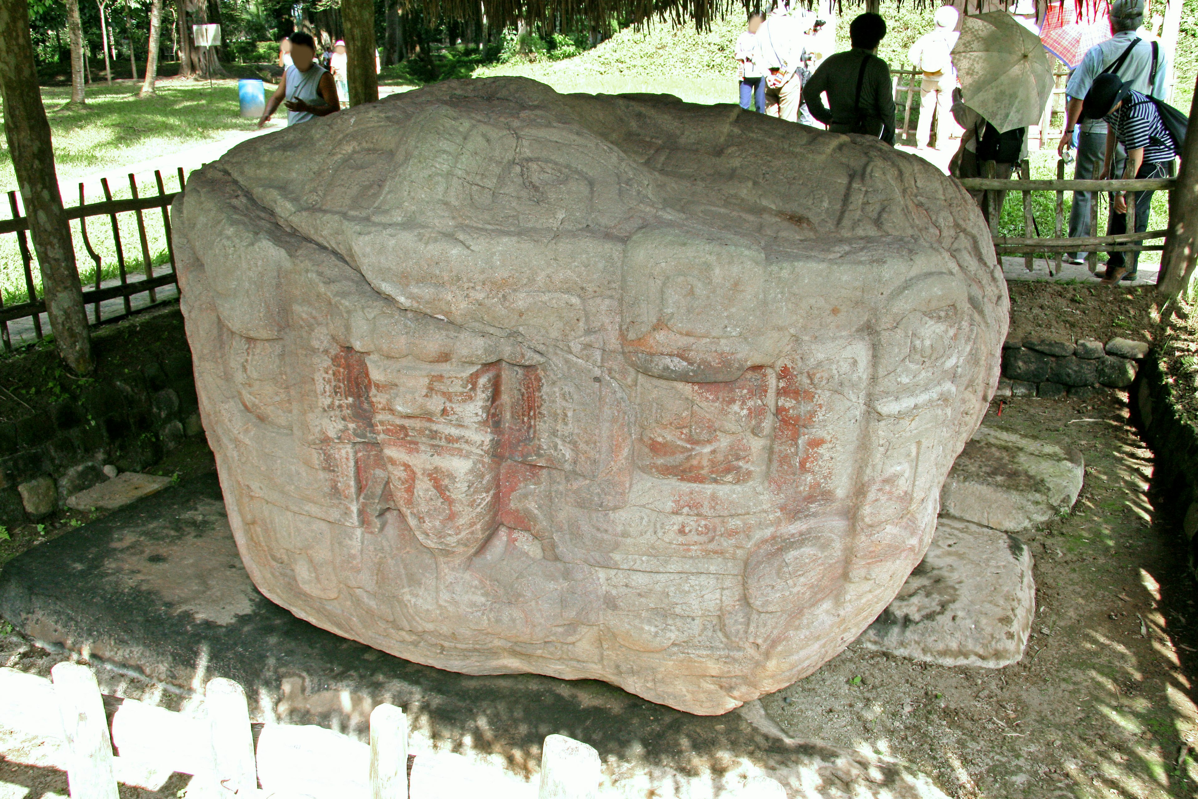 Large stone with ancient carvings surrounded by visitors