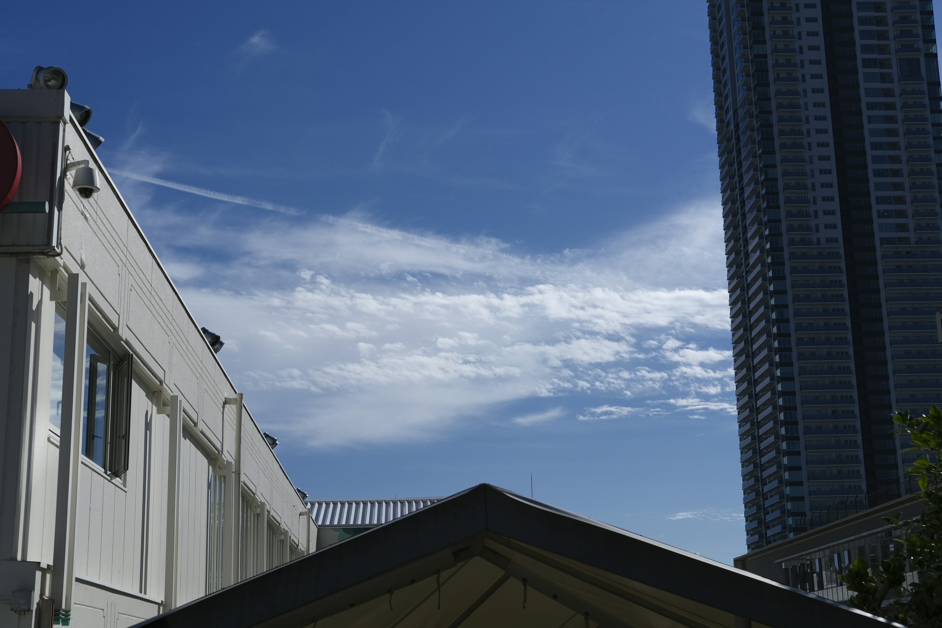 Urban landscape with blue sky and clouds featuring a tall building and white structure