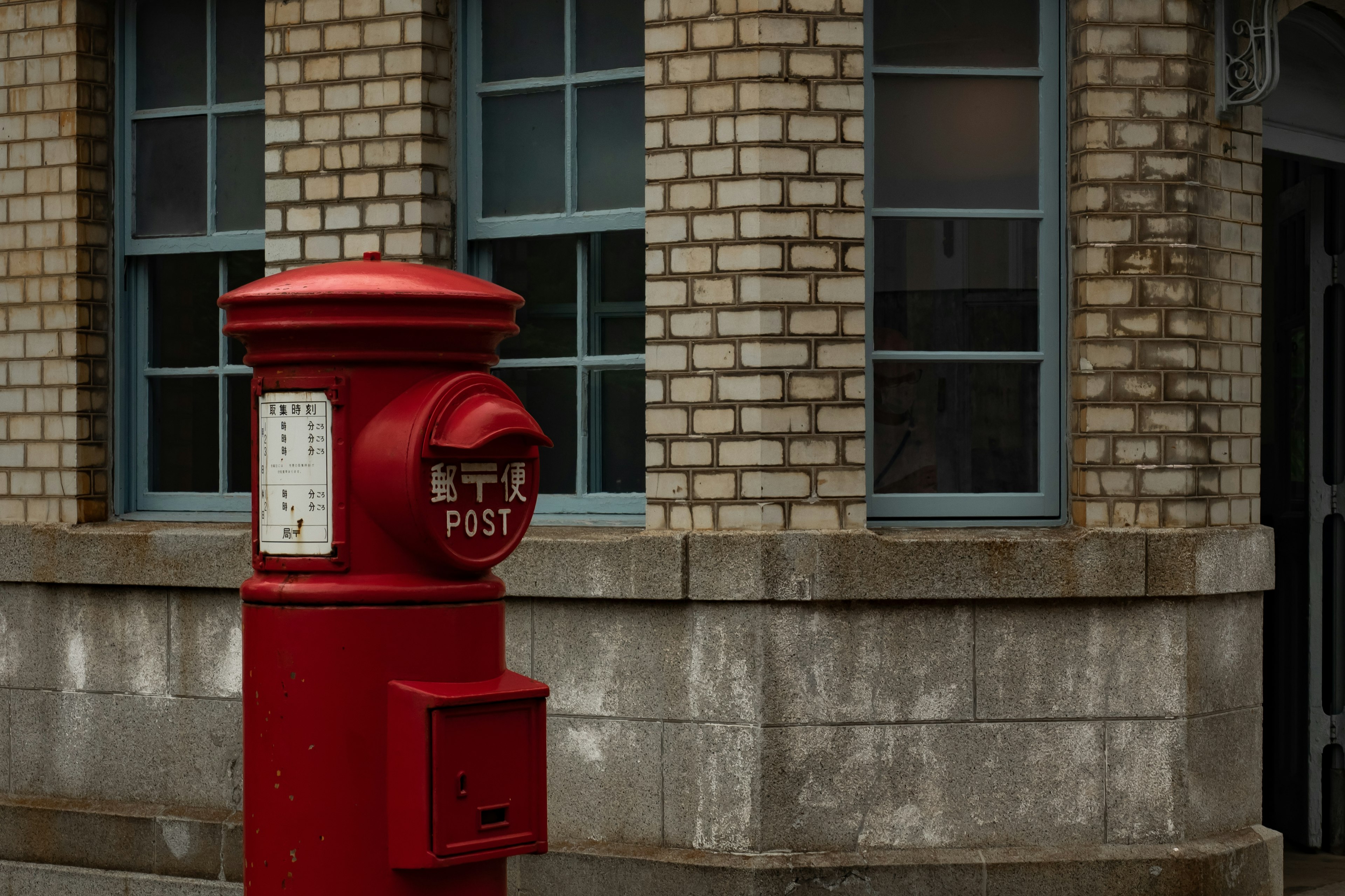 Boîte aux lettres rouge près d'un bâtiment en briques avec des fenêtres bleues