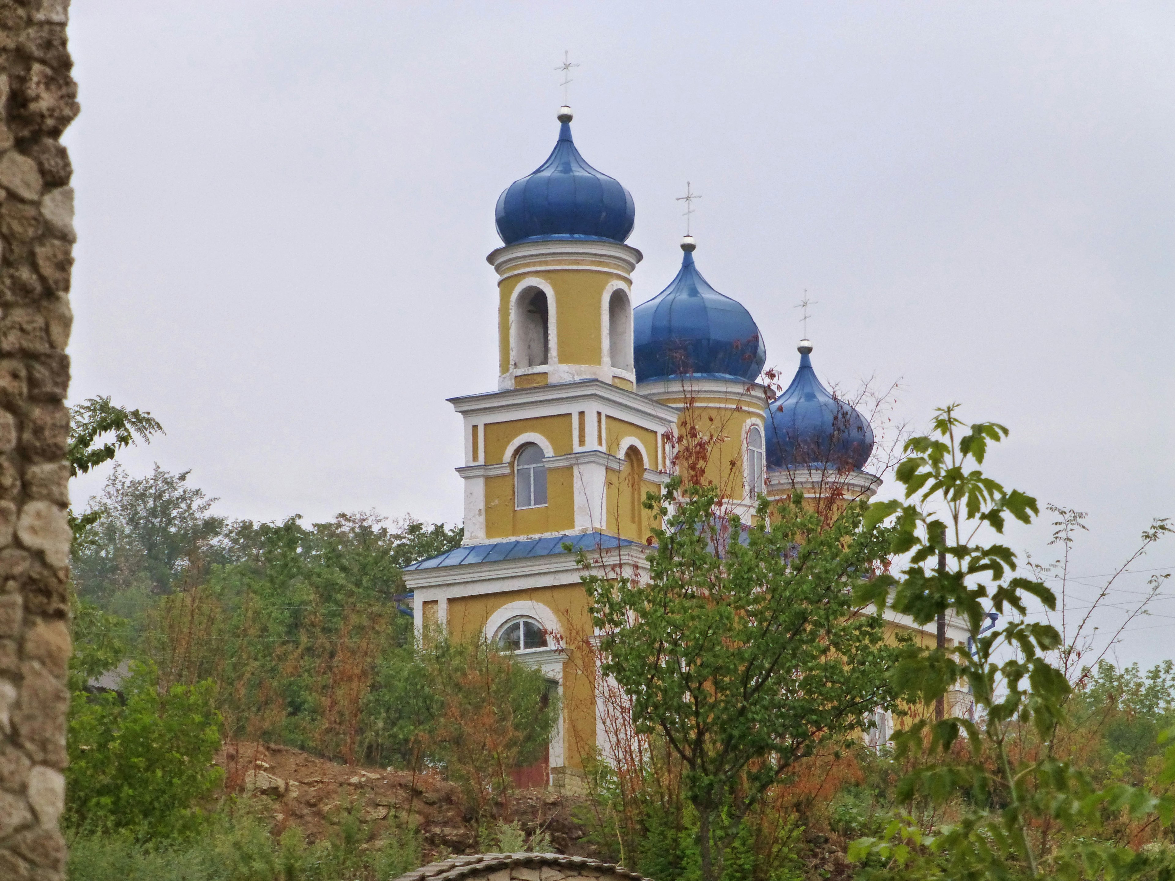 Gelbe Kirche mit blauen Kuppeln umgeben von grünen Bäumen