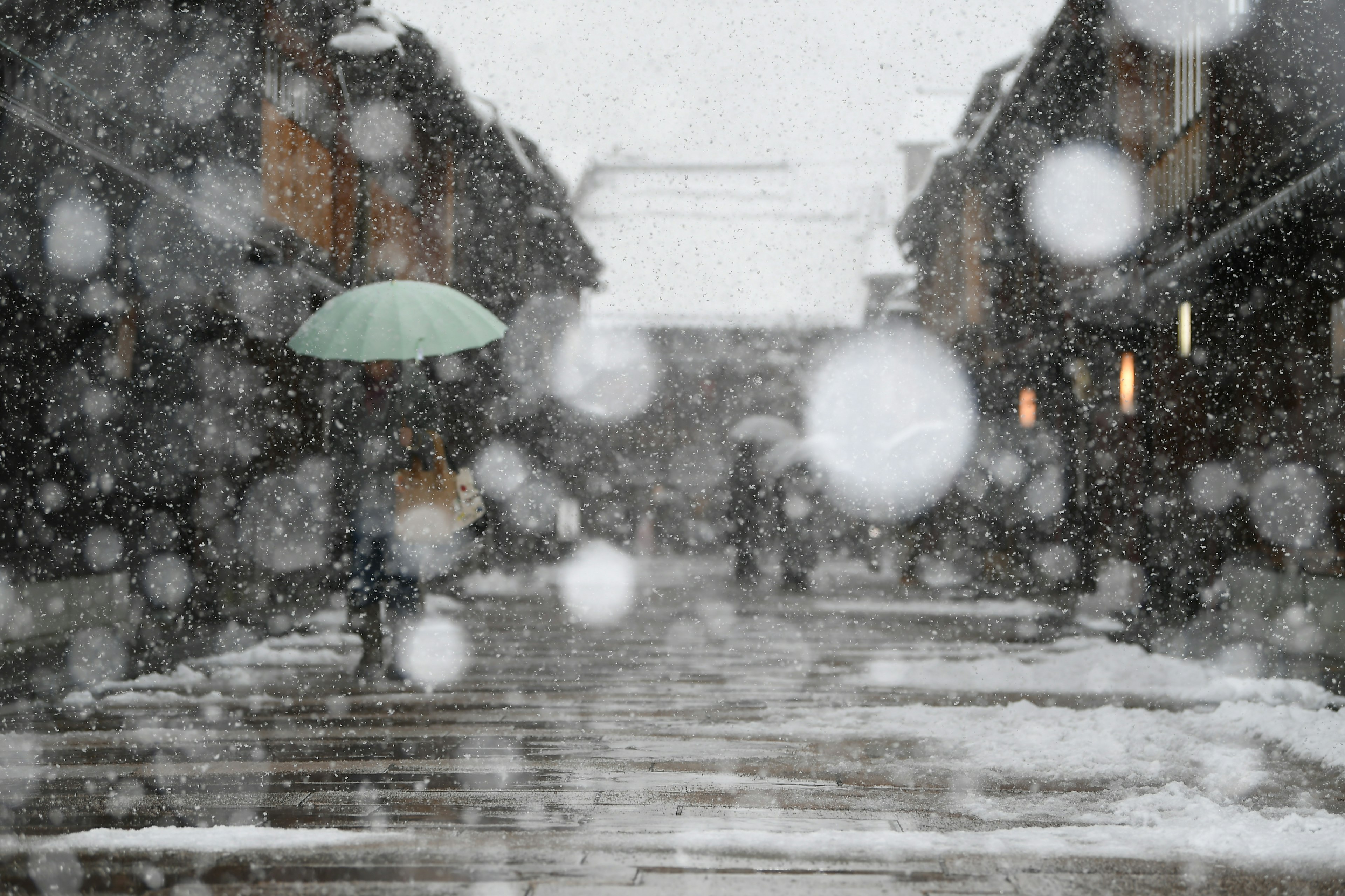 A person with an umbrella walking in the snow amidst an old street scene