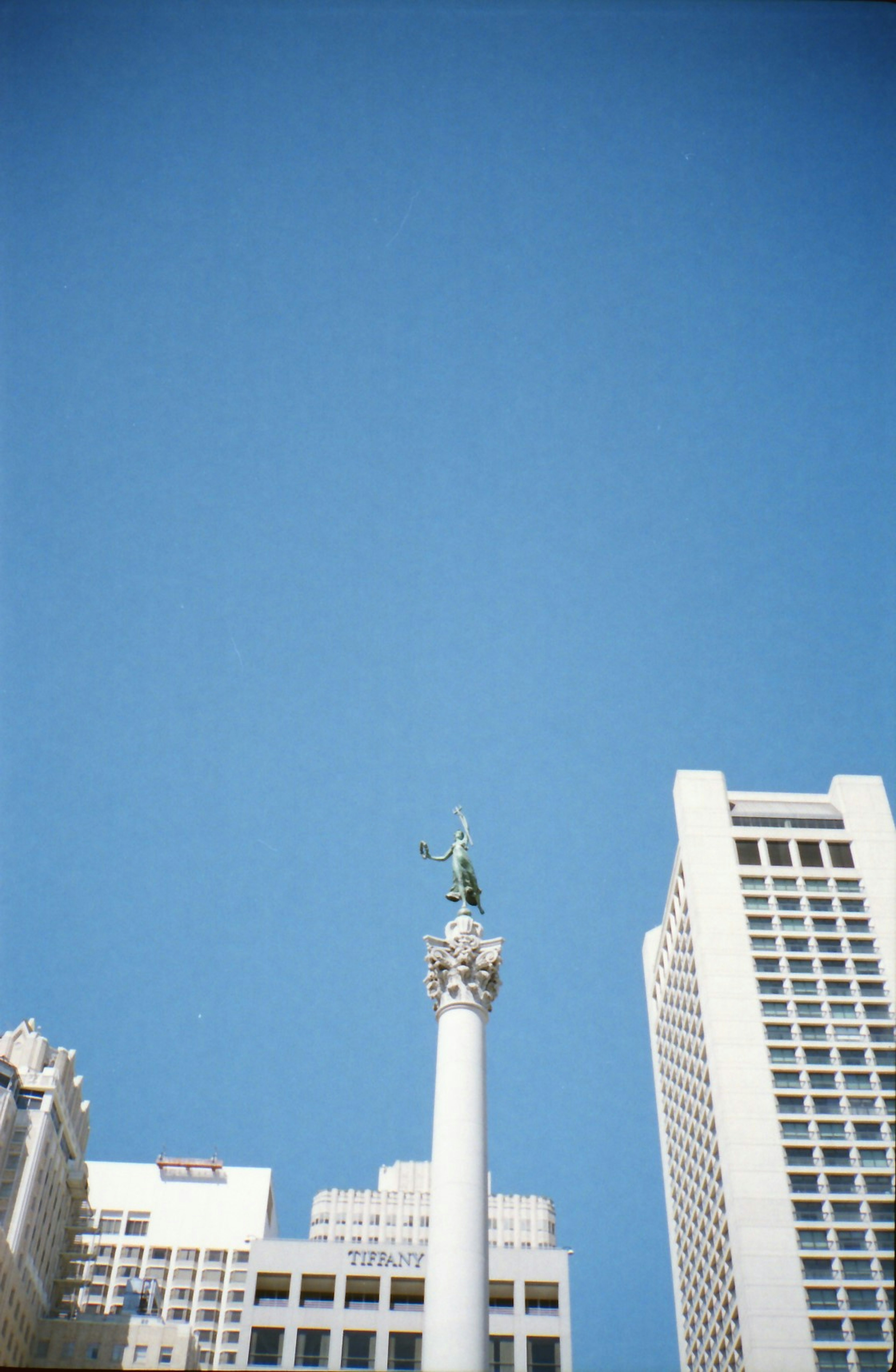 Columna blanca alta bajo un cielo azul claro con edificios circundantes