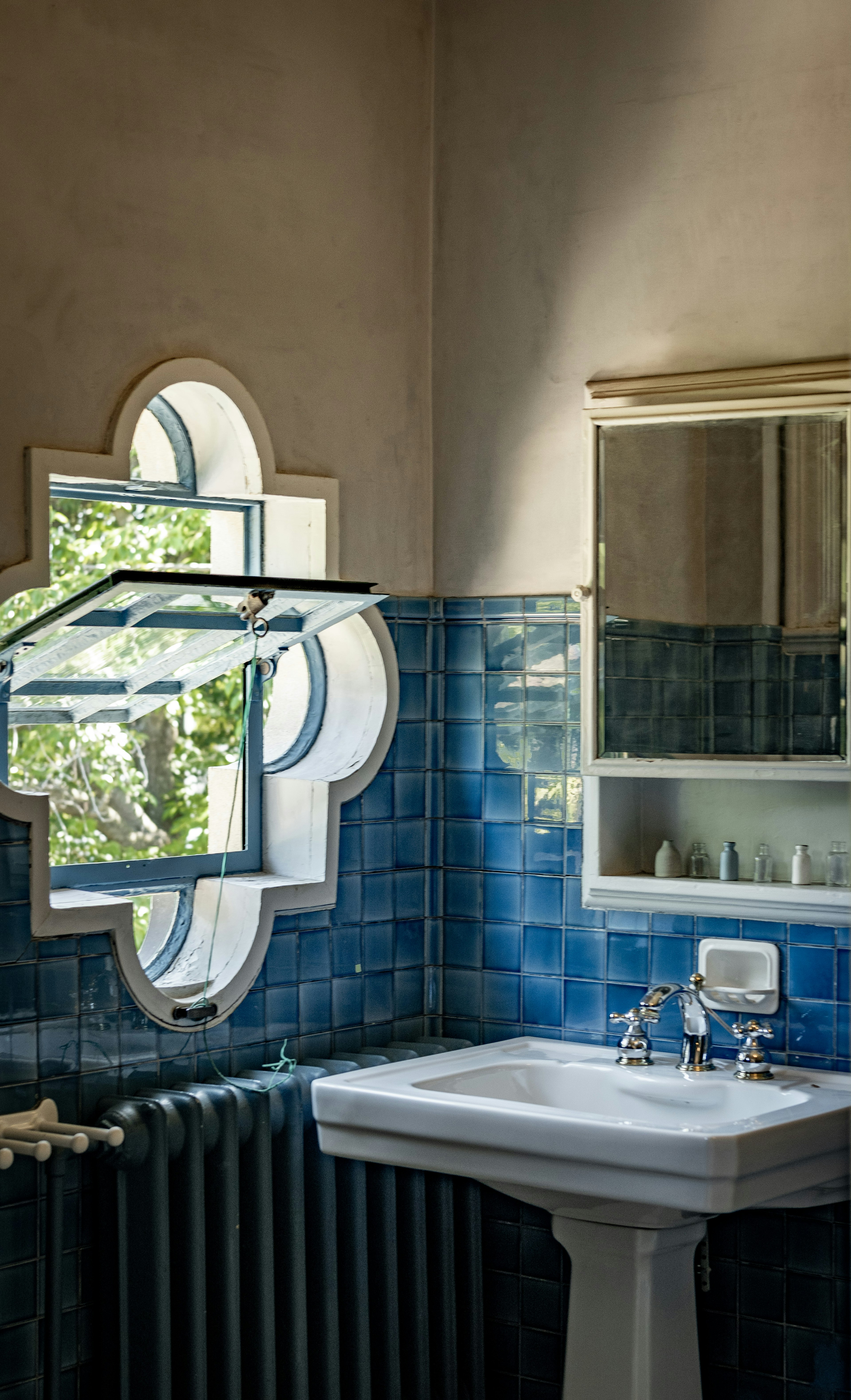 bagno con piastrelle blu e lavabo bianco con finestra a cornice decorativa