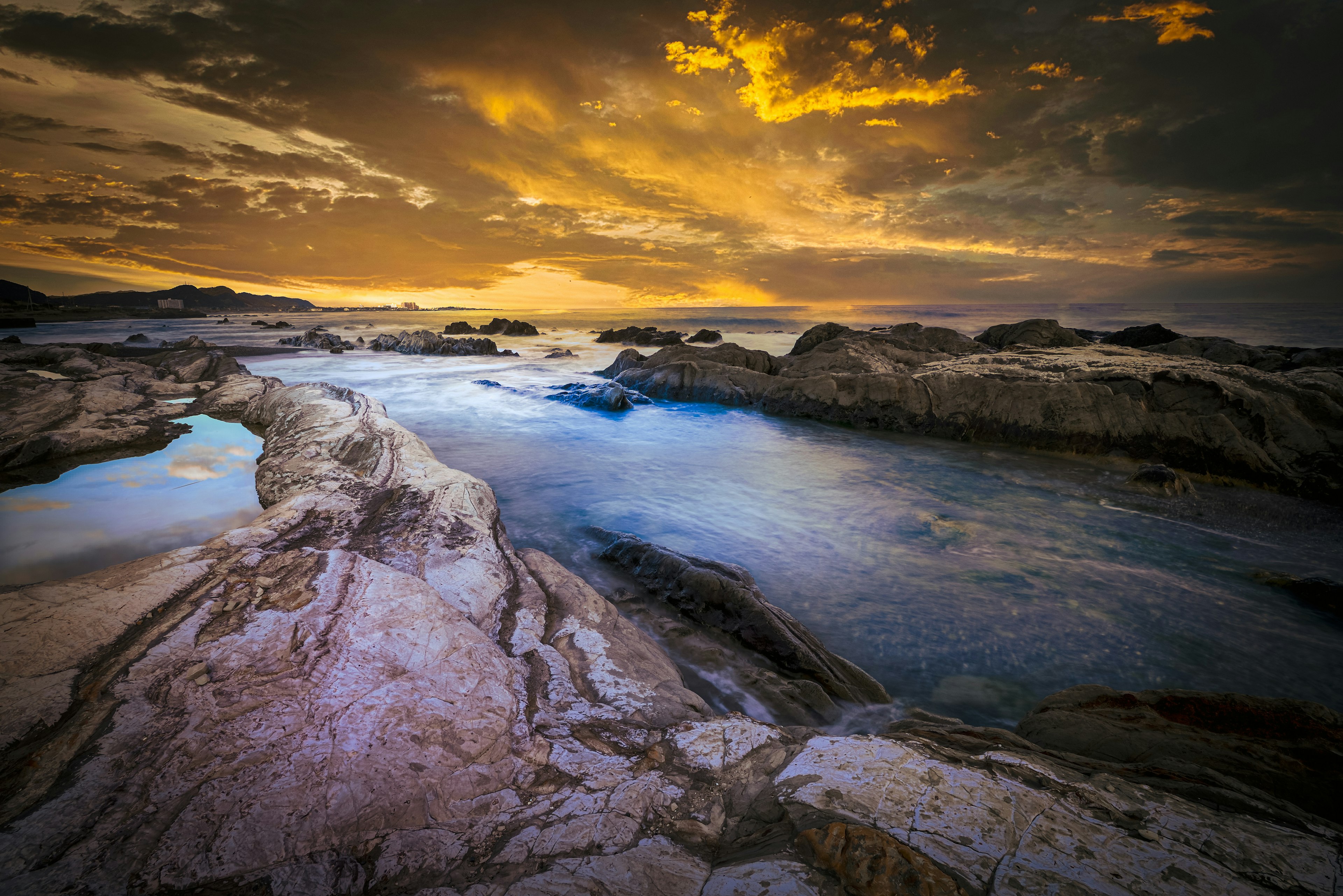 Pemandangan pantai senja yang indah air tenang di antara batu