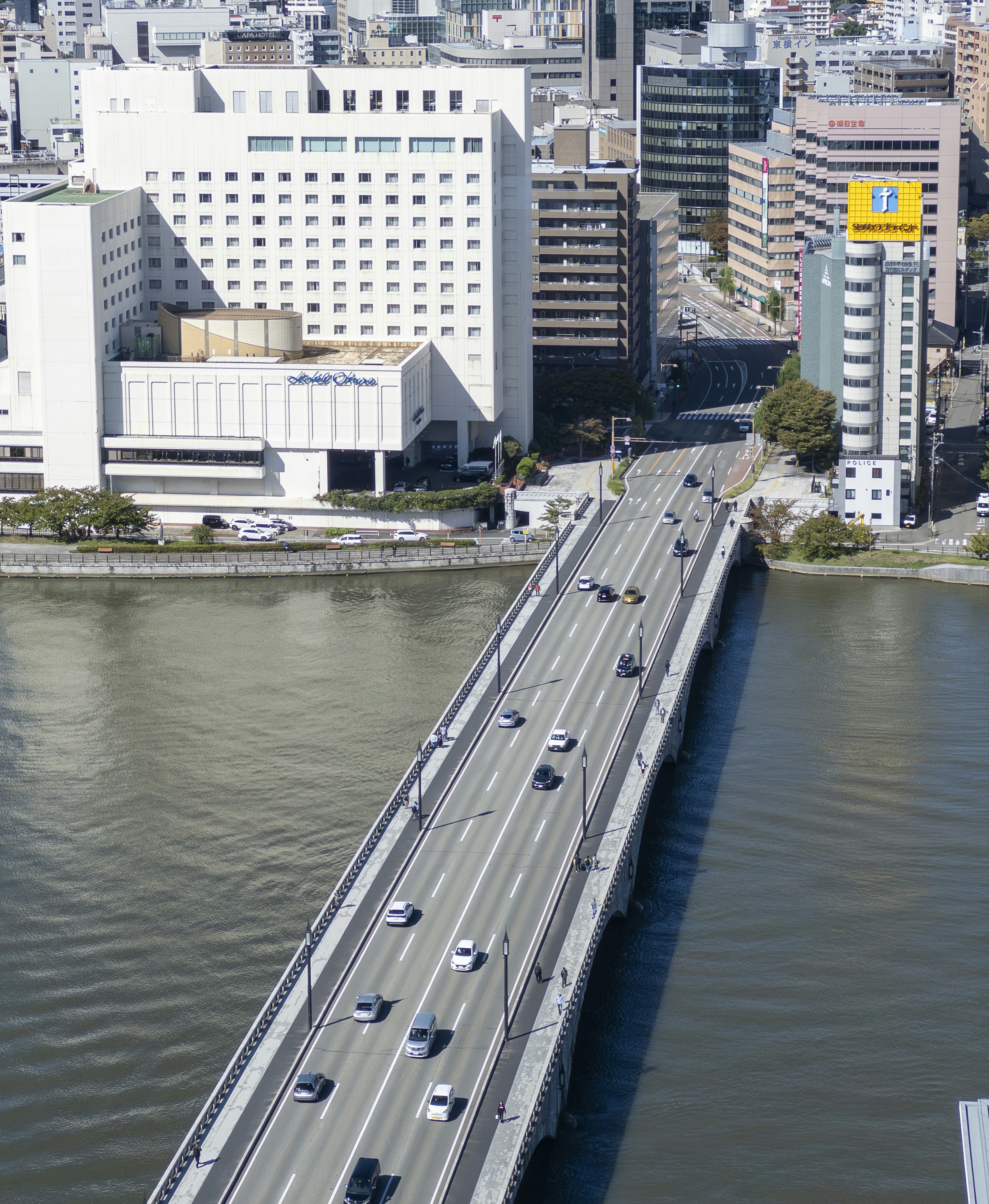 A bridge over a river with cars driving on it and city buildings in the background