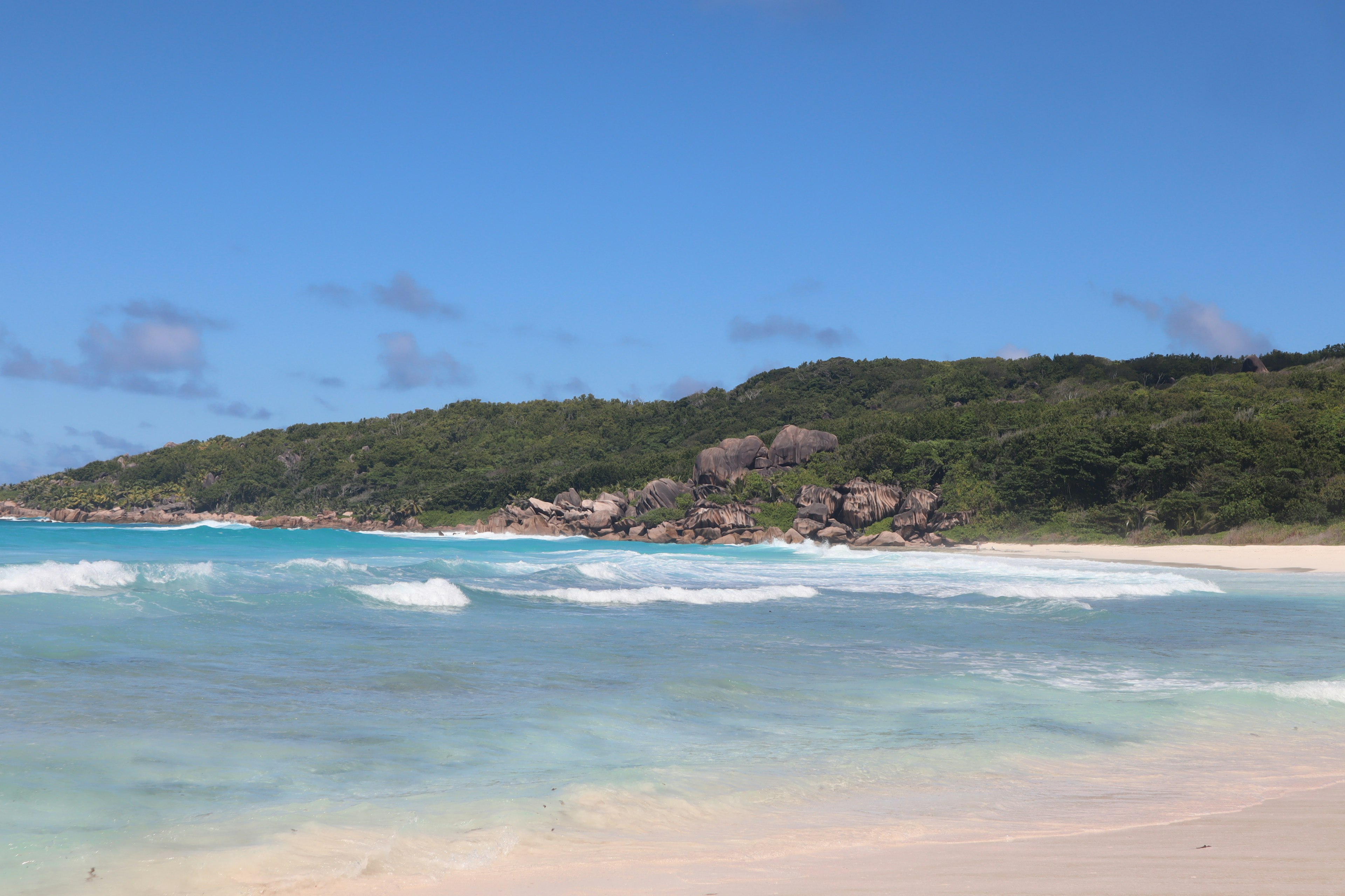 ชายหาดที่สวยงามพร้อมคลื่นทะเลสีน้ำเงินและเนินเขาสีเขียวในพื้นหลัง