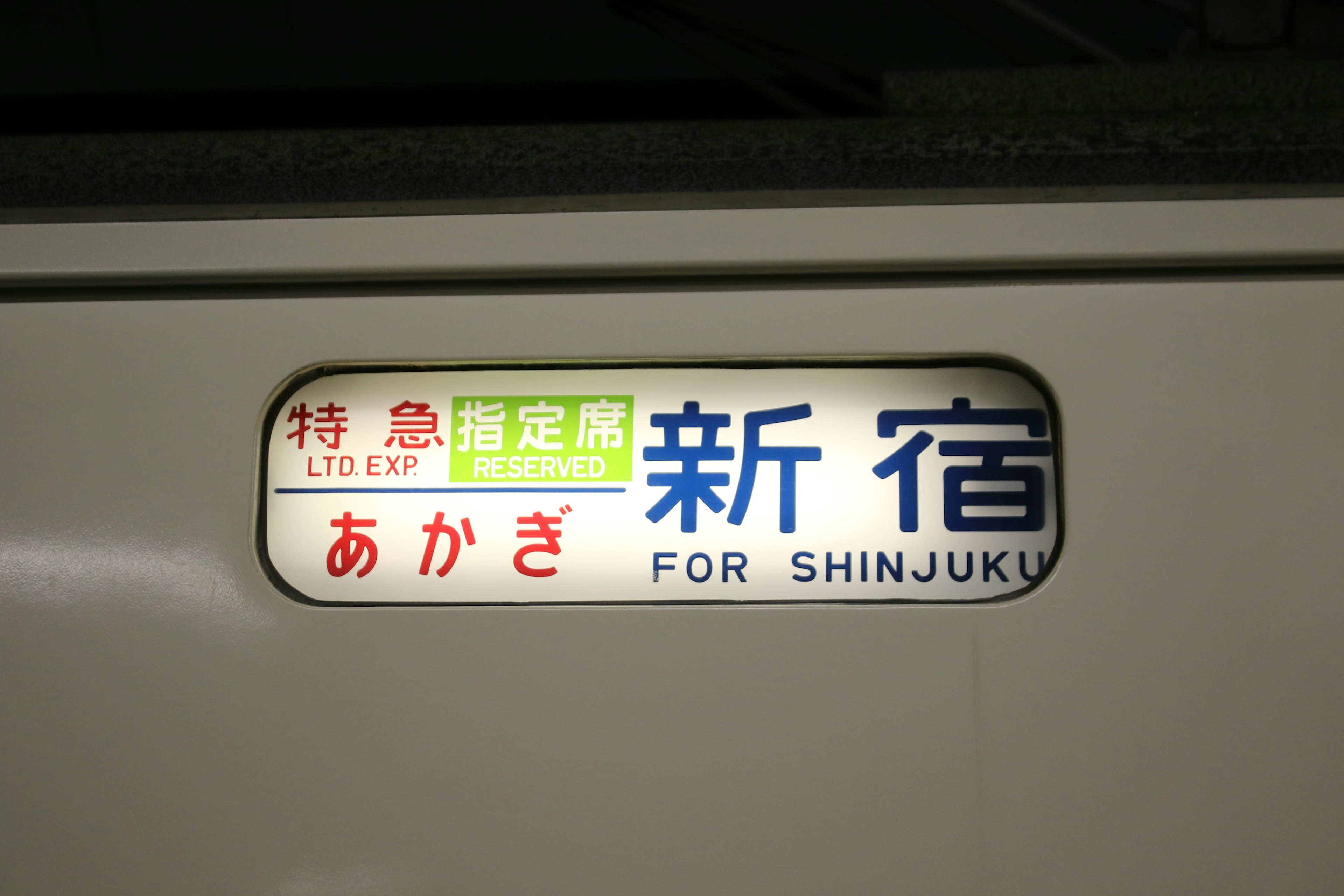 Cartel del tren hacia Shinjuku con fondo azul y verde y texto blanco