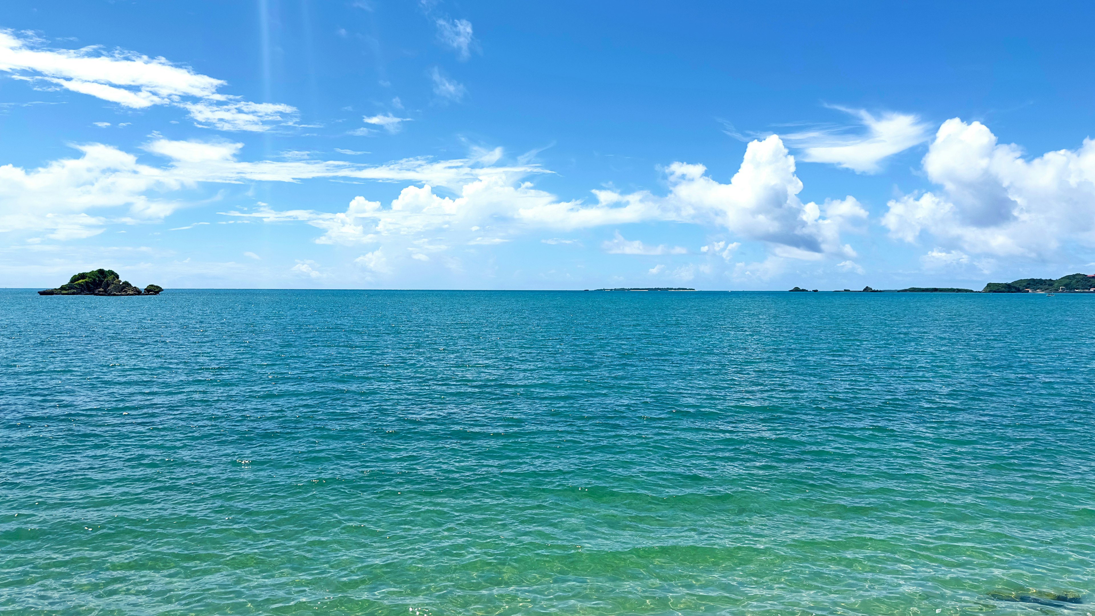 Vast blue ocean under a bright sky with fluffy white clouds and a small island