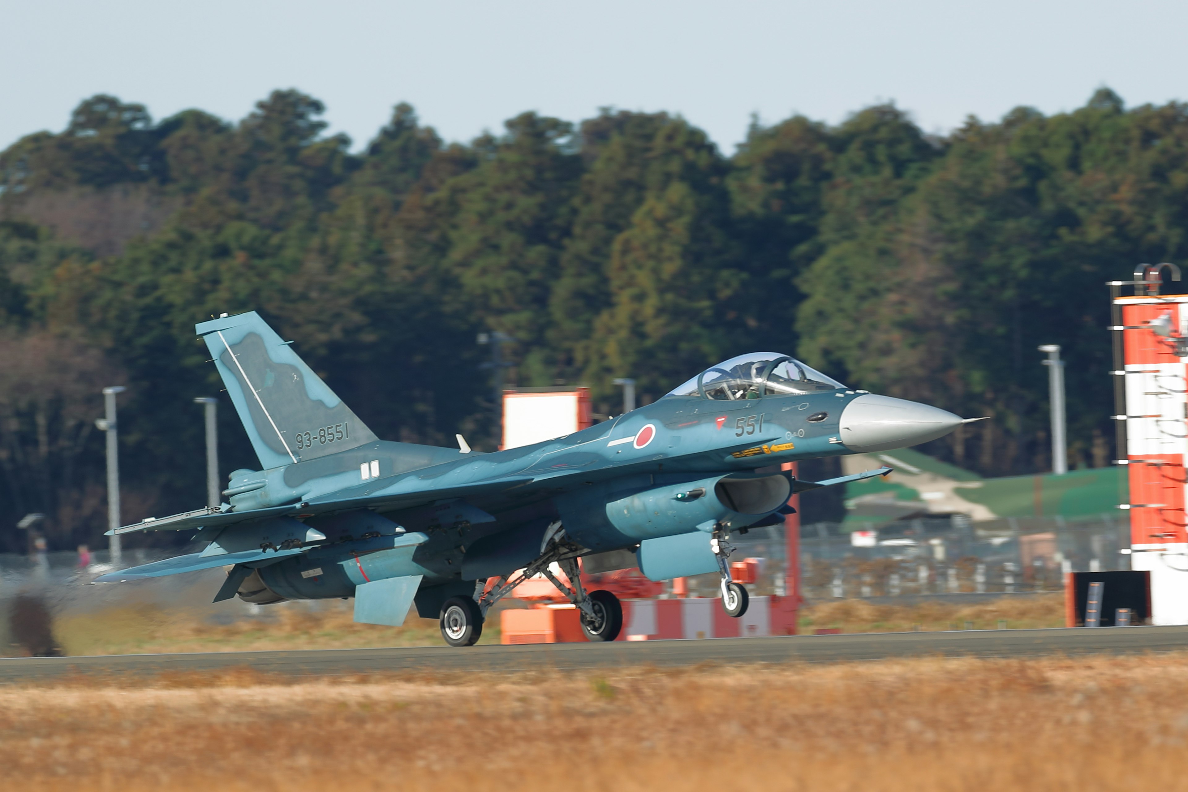 A fighter jet taking off with a teal color scheme and runway in the background