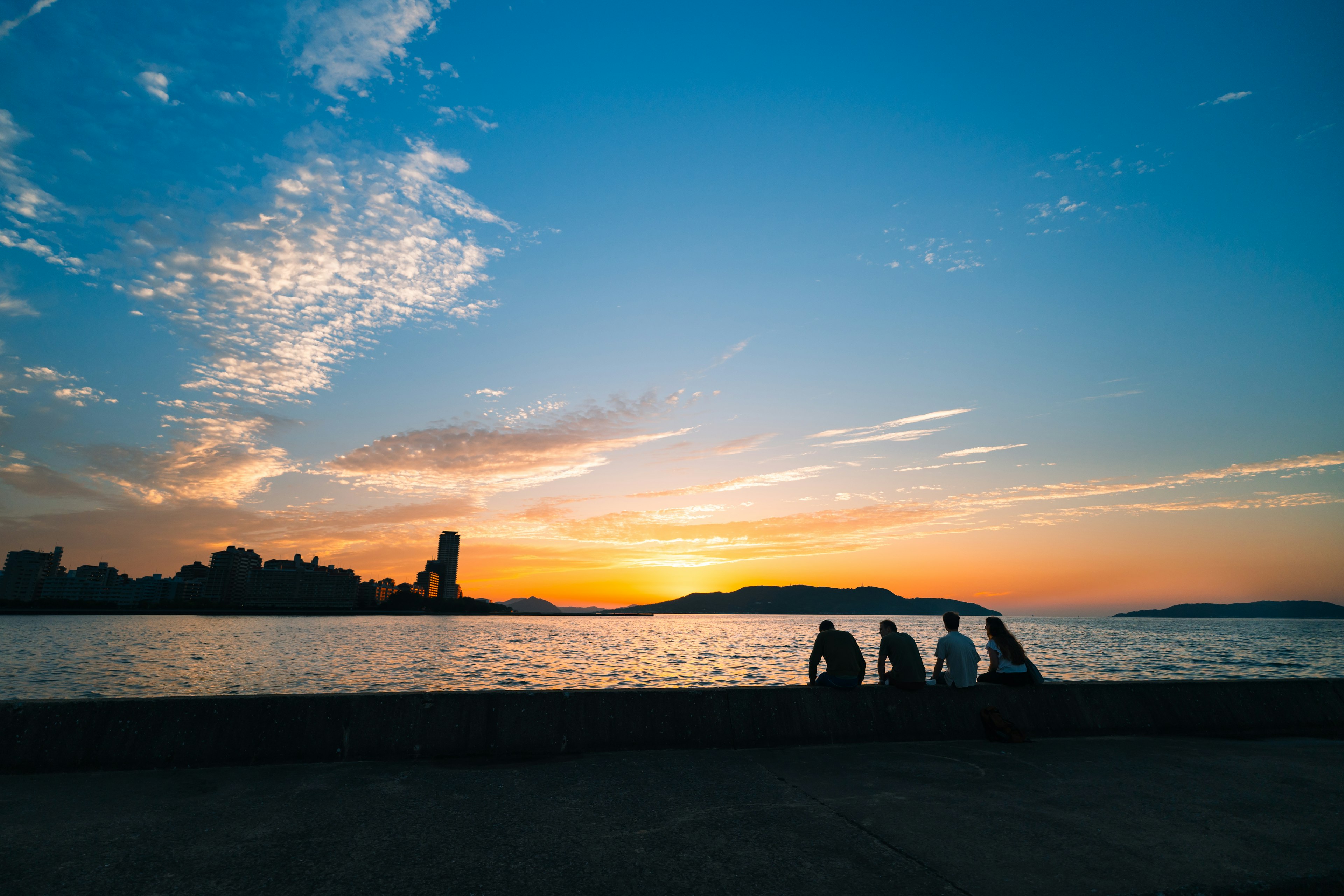 夕日を背景に海辺に座る人々のシルエット