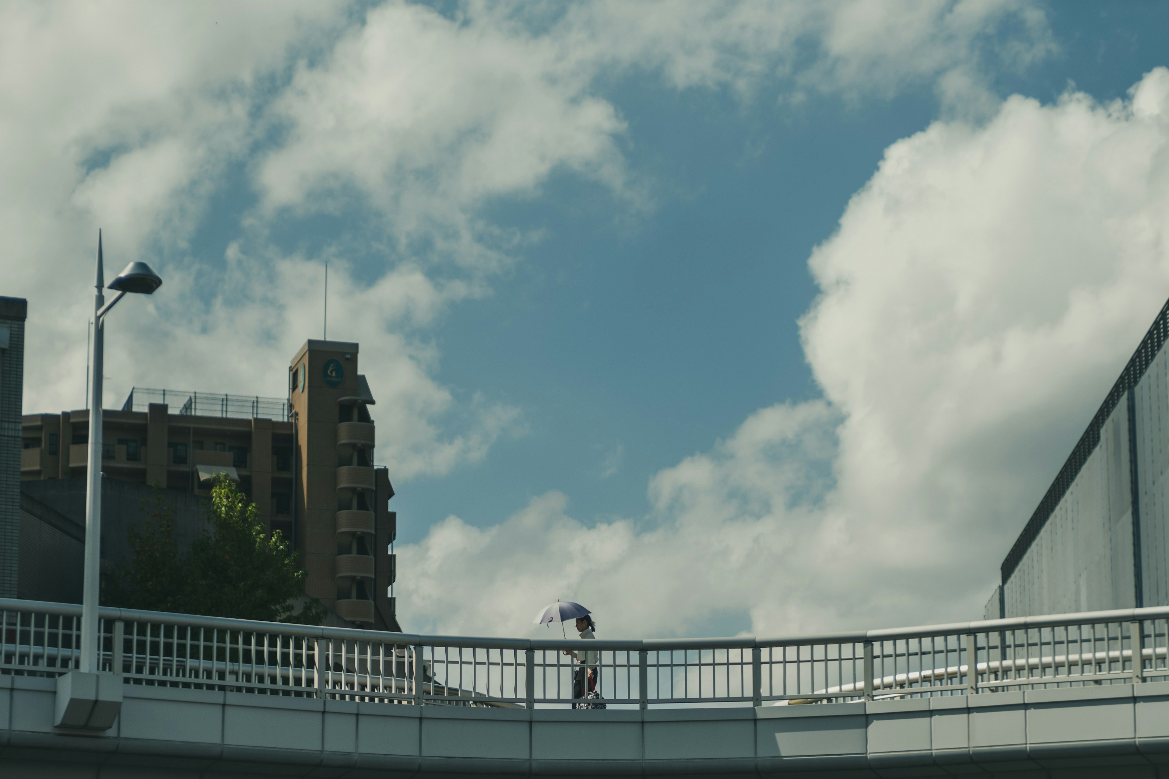 Person walking on pedestrian bridge under blue sky with clouds