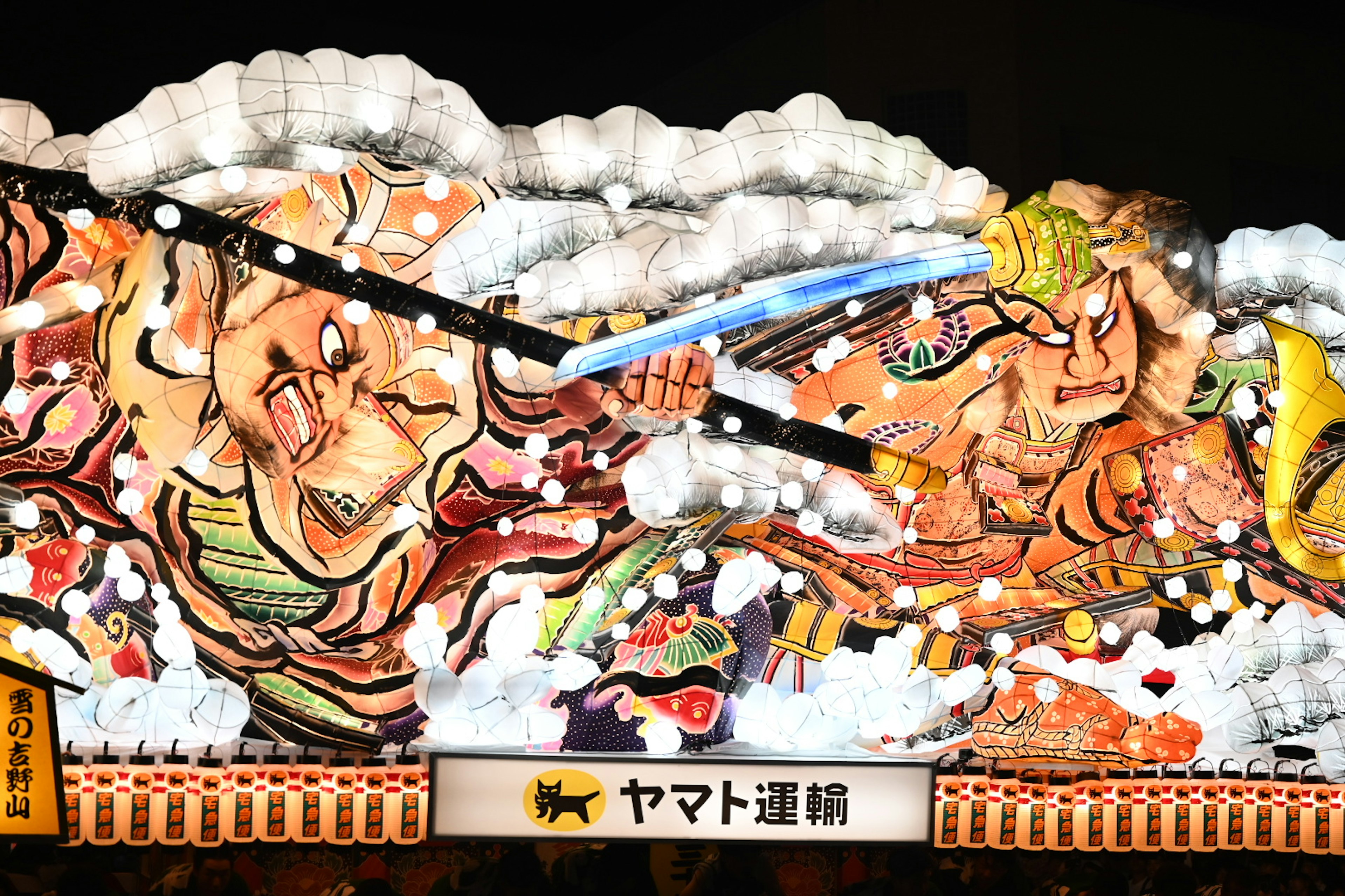 Night festival float depicting a samurai battle scene illuminated with lights