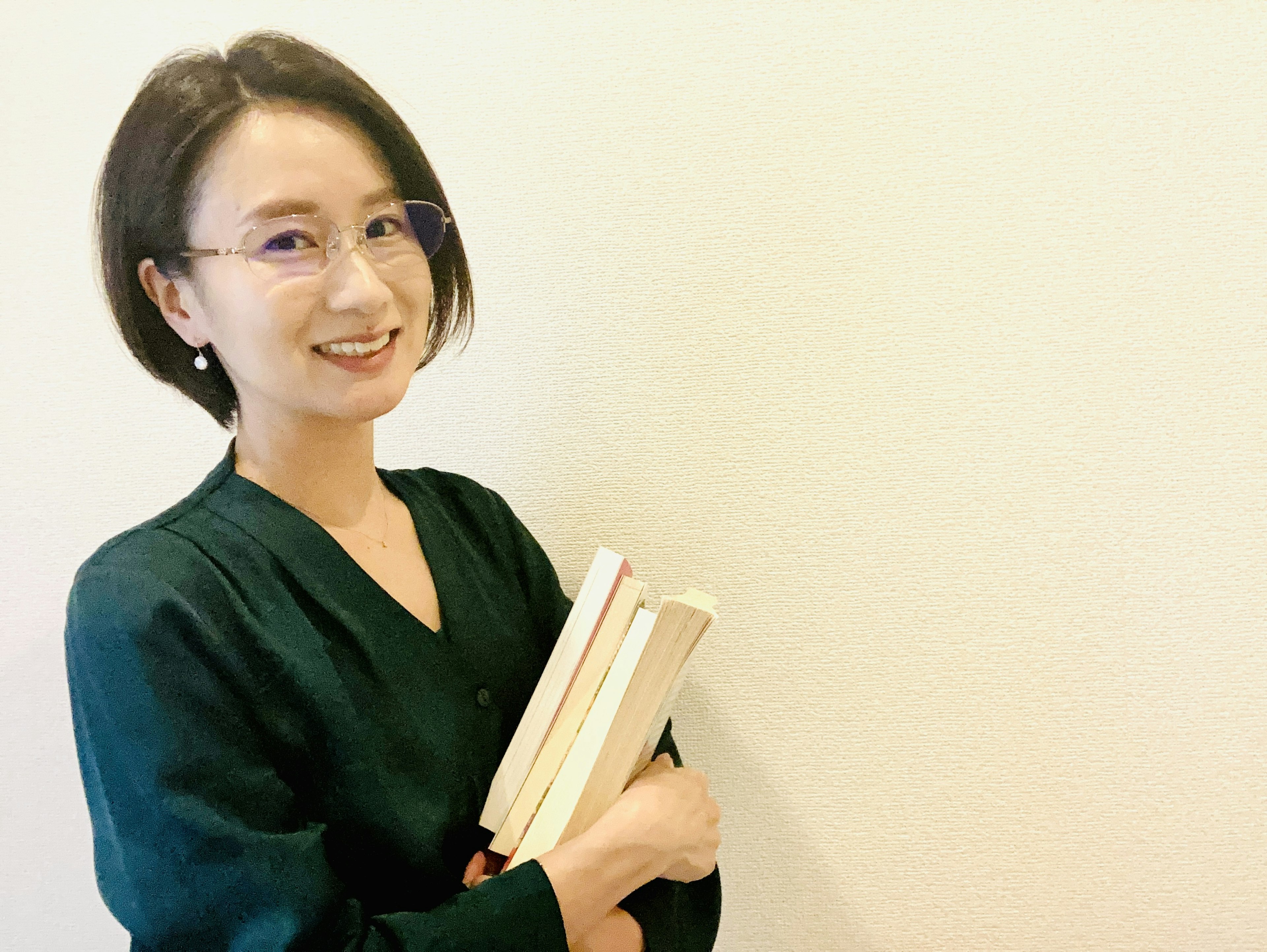 Mujer sonriente con cabello corto sosteniendo libros contra un fondo simple