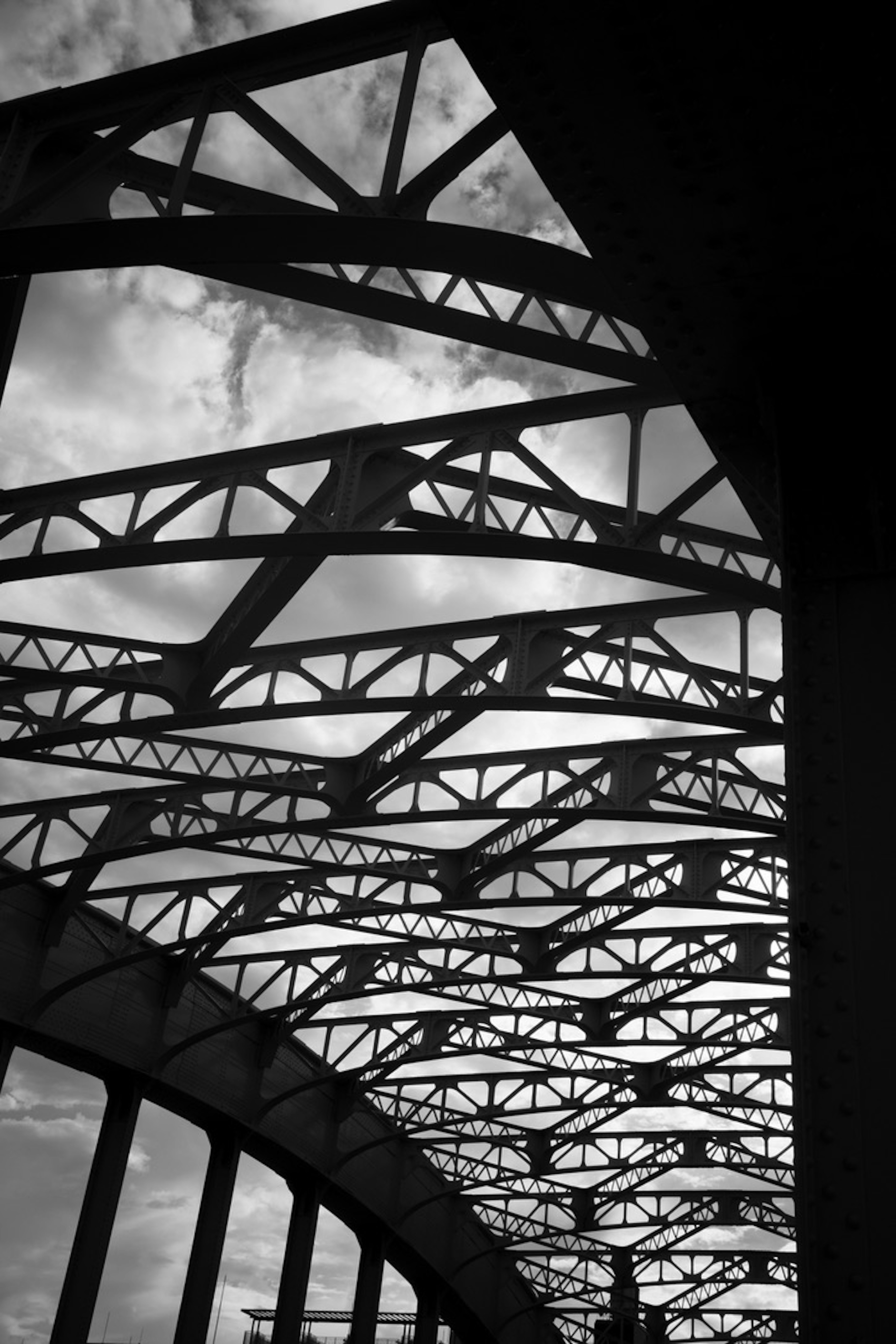 Foto hitam putih dari struktur jembatan yang menunjukkan truss baja dan langit