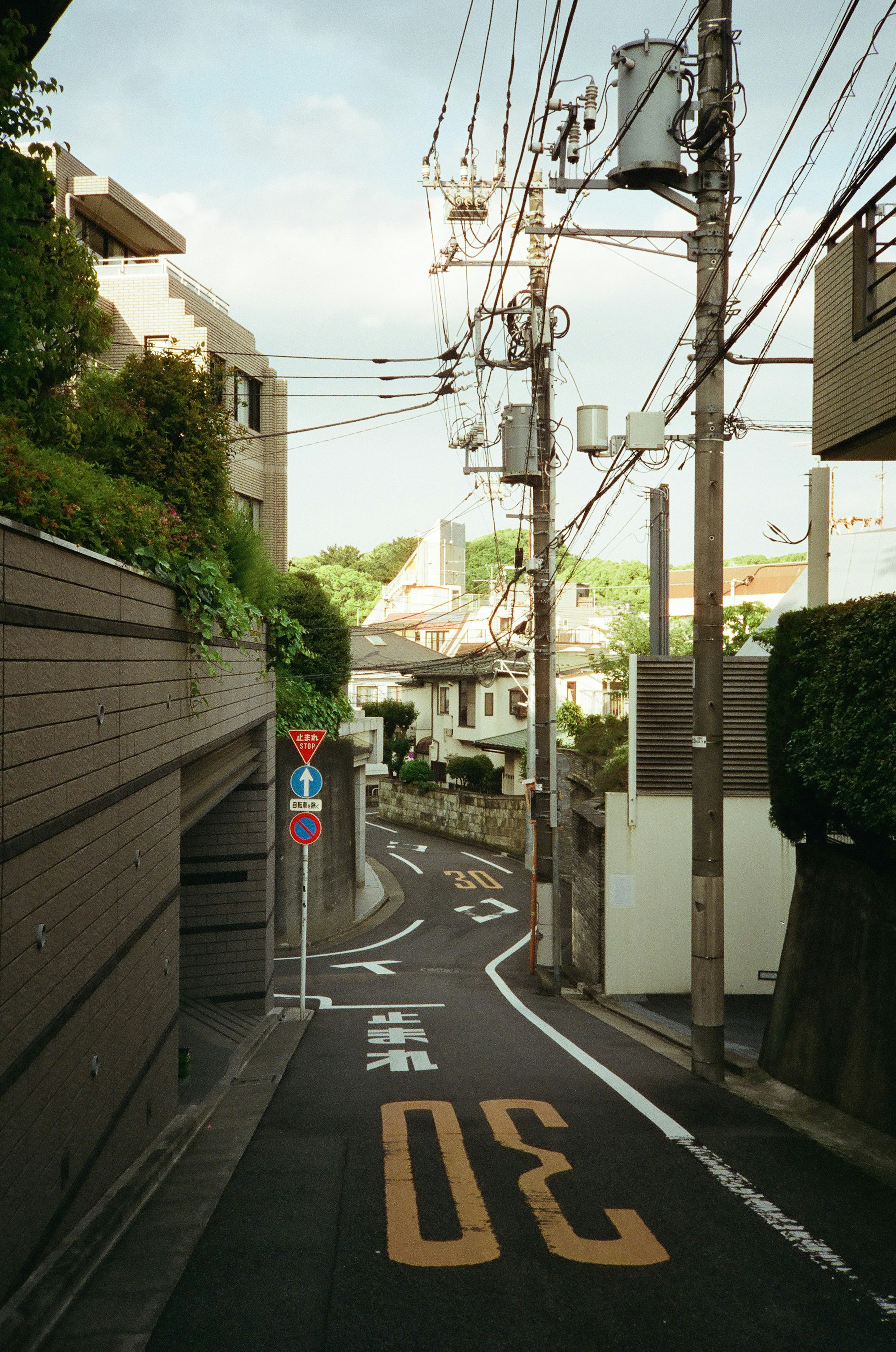 Narrow street scene with residential buildings visible, featuring road signs and power lines