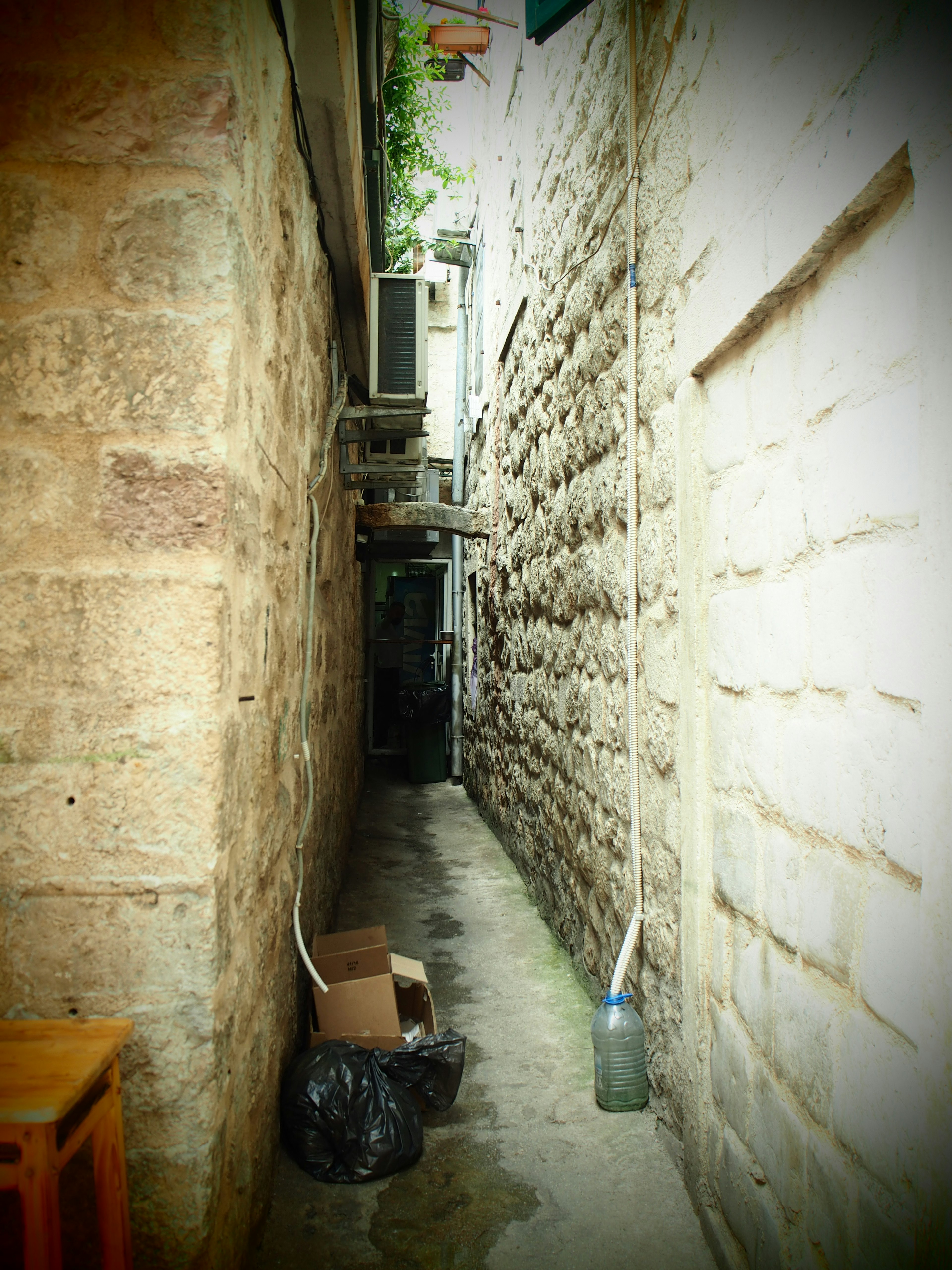 Allée étroite avec des murs en pierre et des sacs poubelles