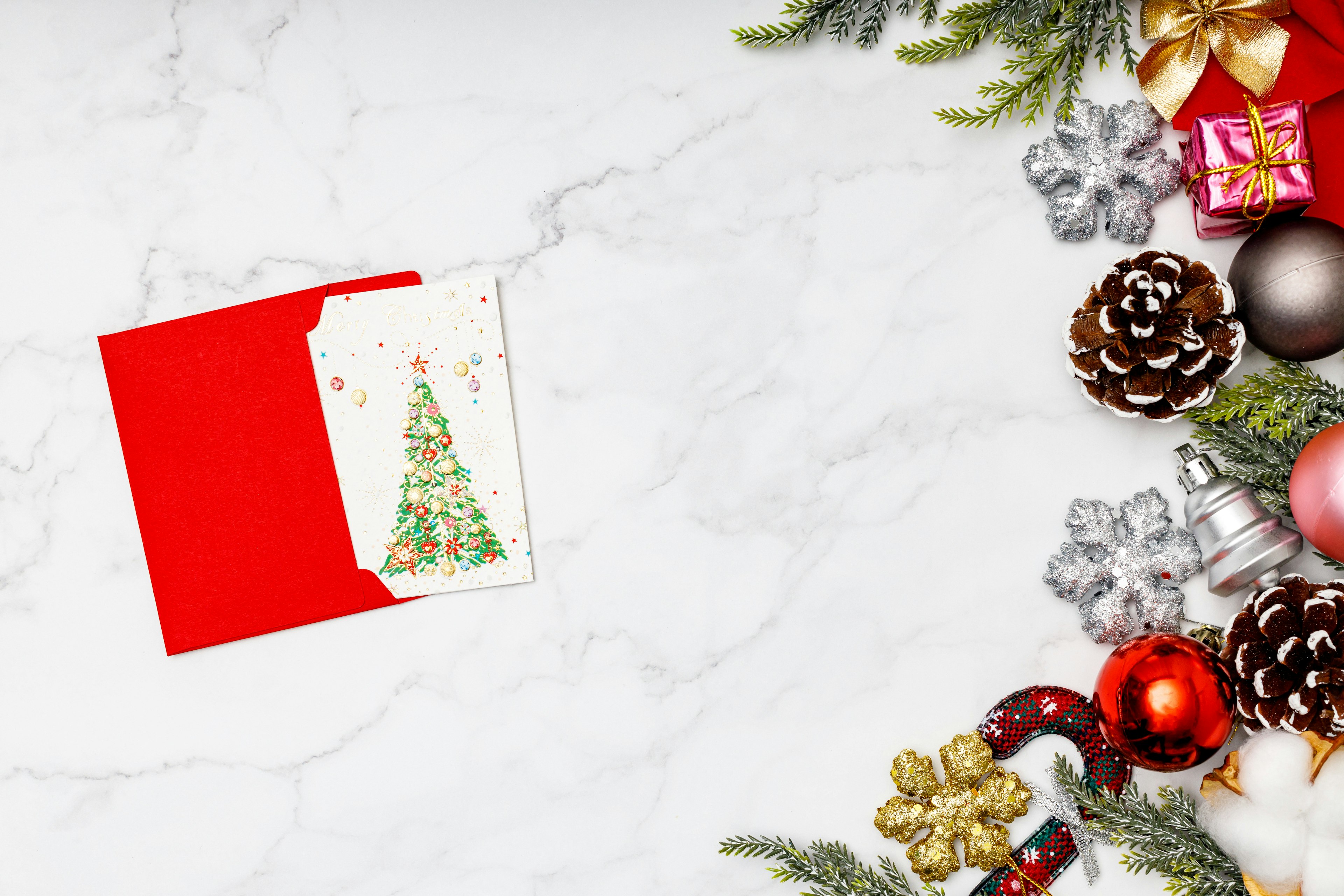 Une enveloppe rouge avec une carte illustrée d'un sapin de Noël entourée de décorations festives