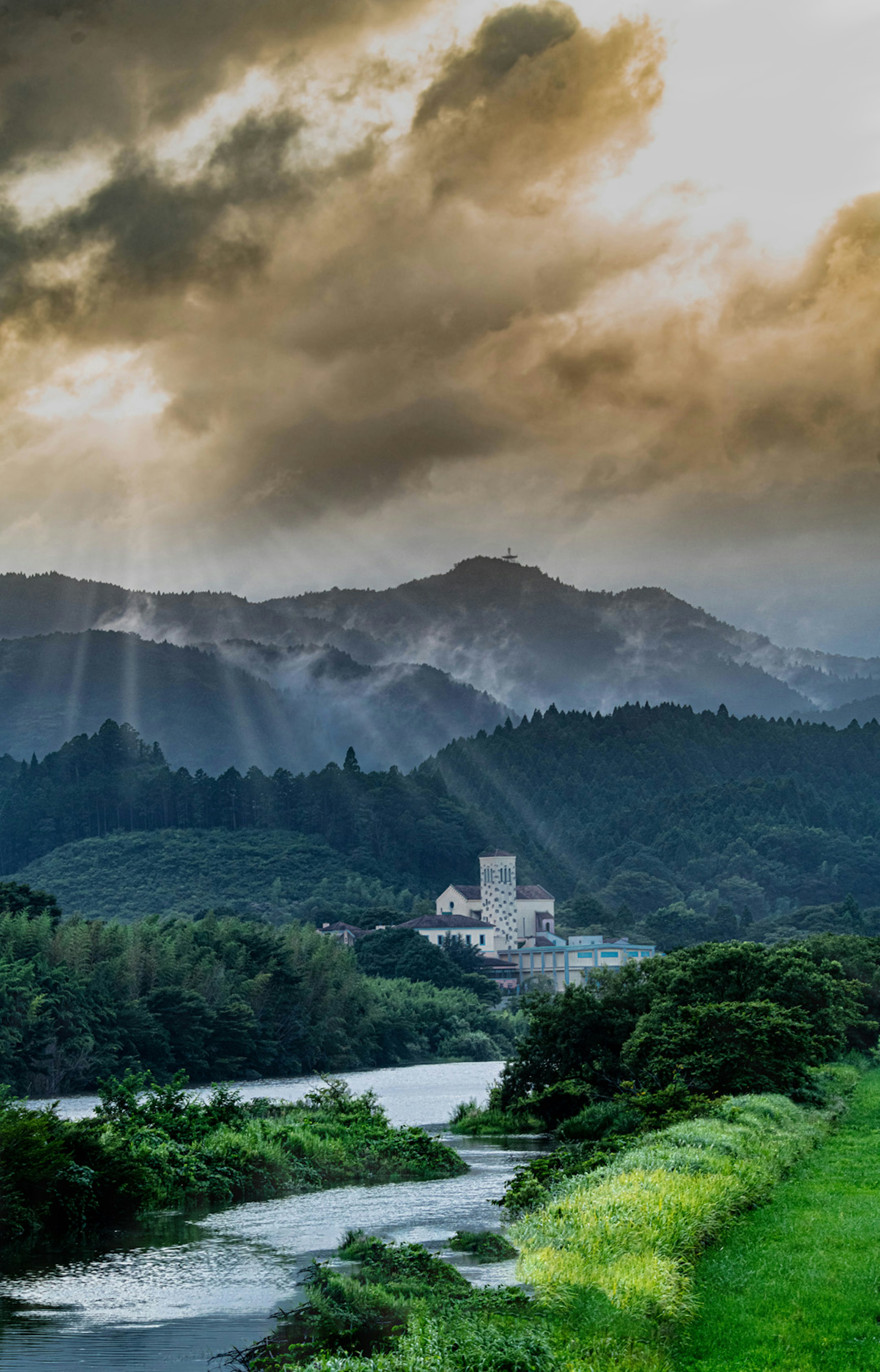 Vista escénica de montañas y río con rayos de sol atravesando las nubes