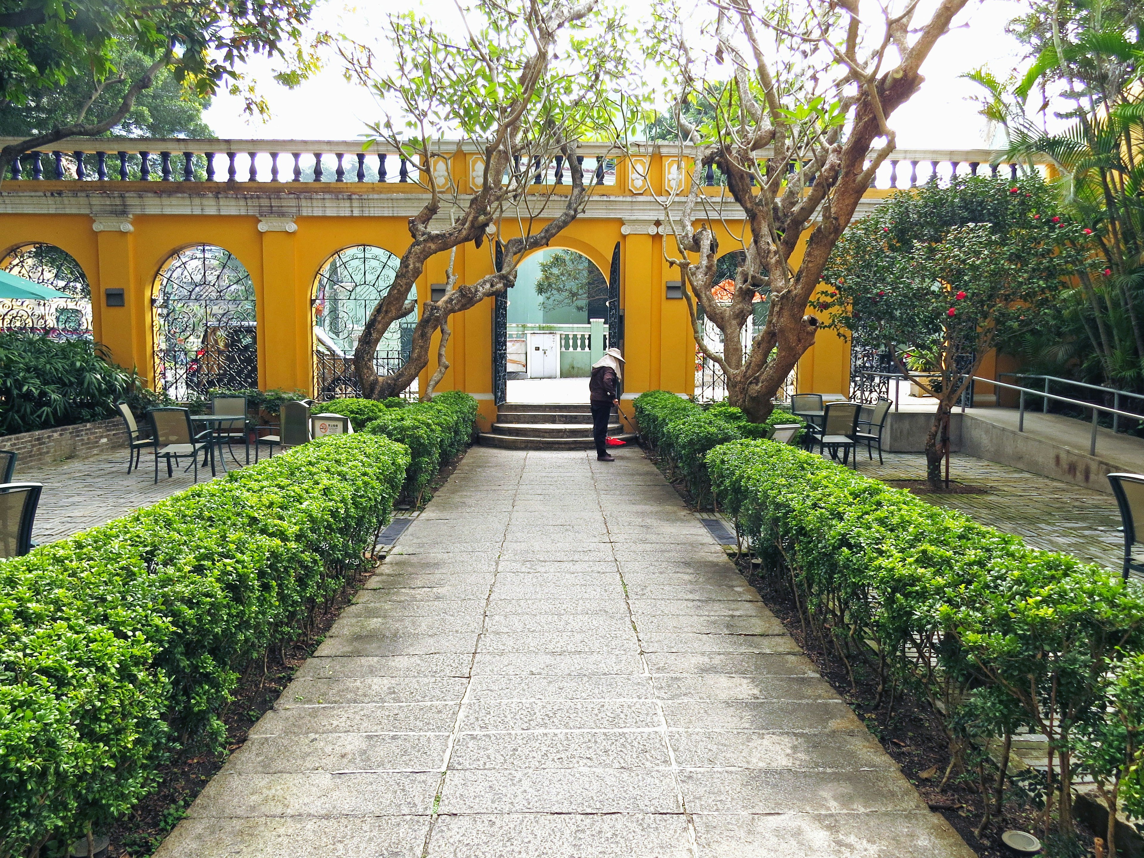 Un hermoso camino de jardín centrado con un edificio amarillo y arbustos verdes exuberantes