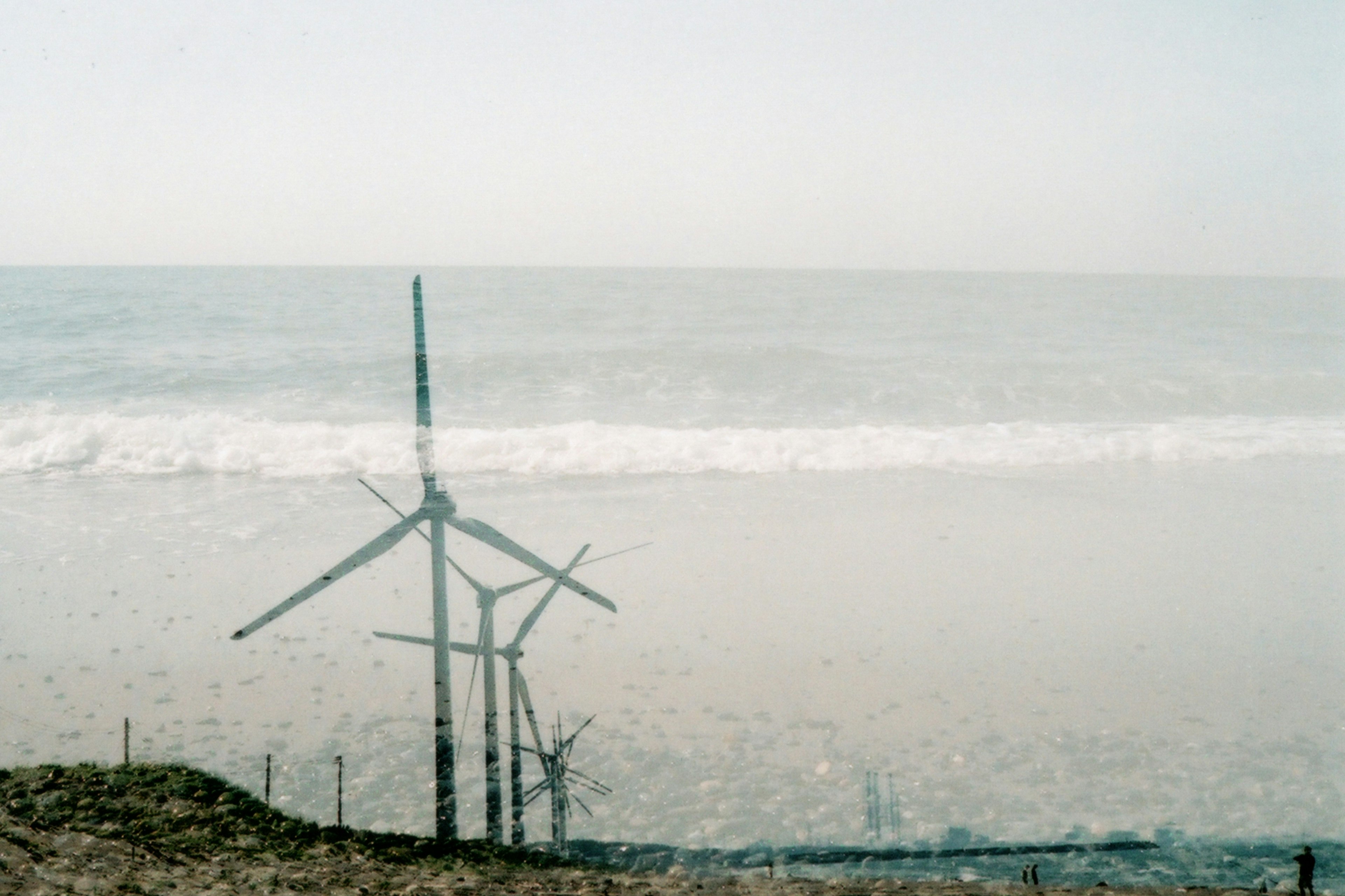 Silhouette von Windkraftanlagen, die dem Meer zugewandt sind, mit sanften Wellen im Hintergrund