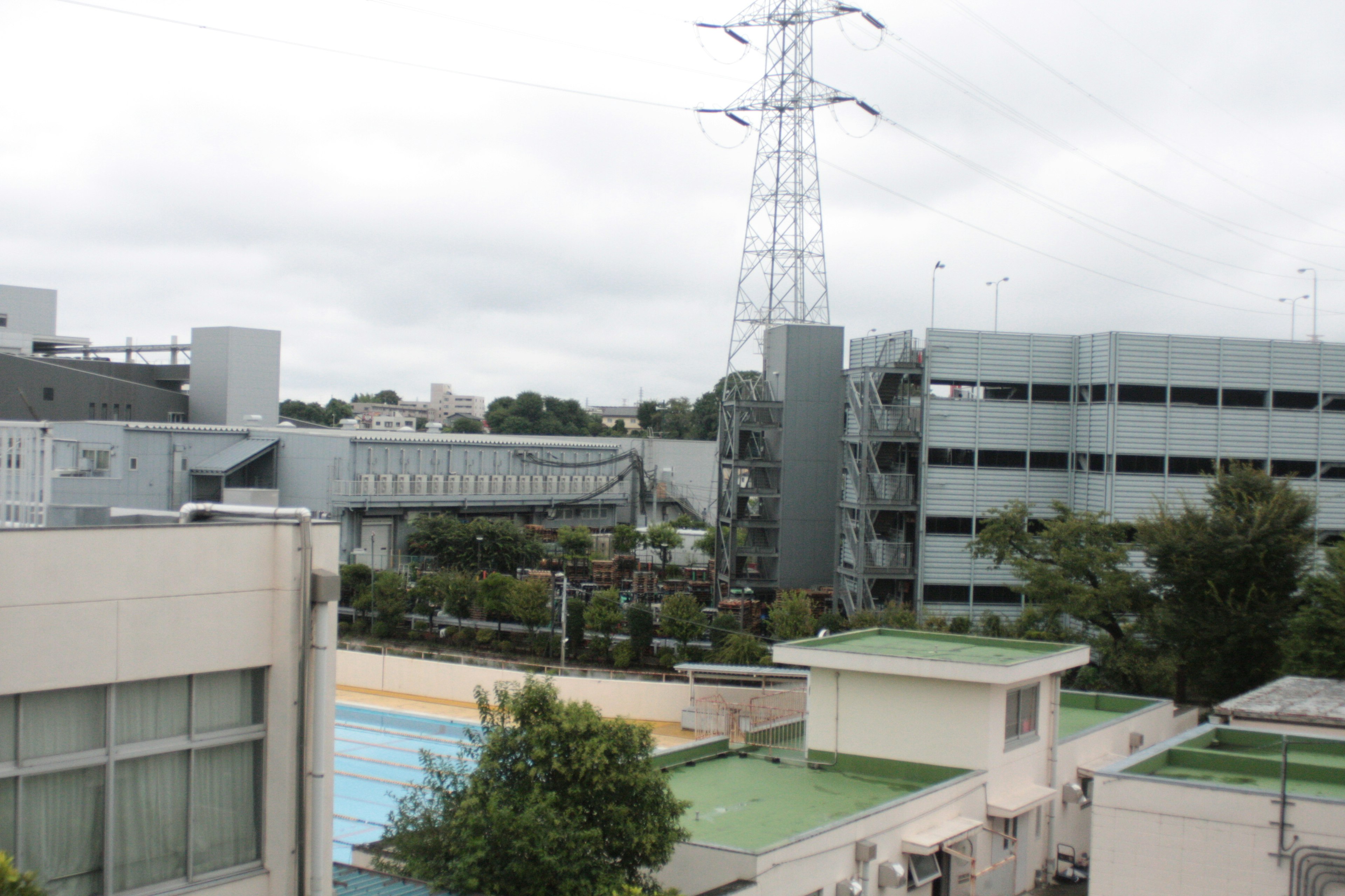 屋外のプールと近代的な建物が見える風景 高い電柱と緑の植栽が特徴