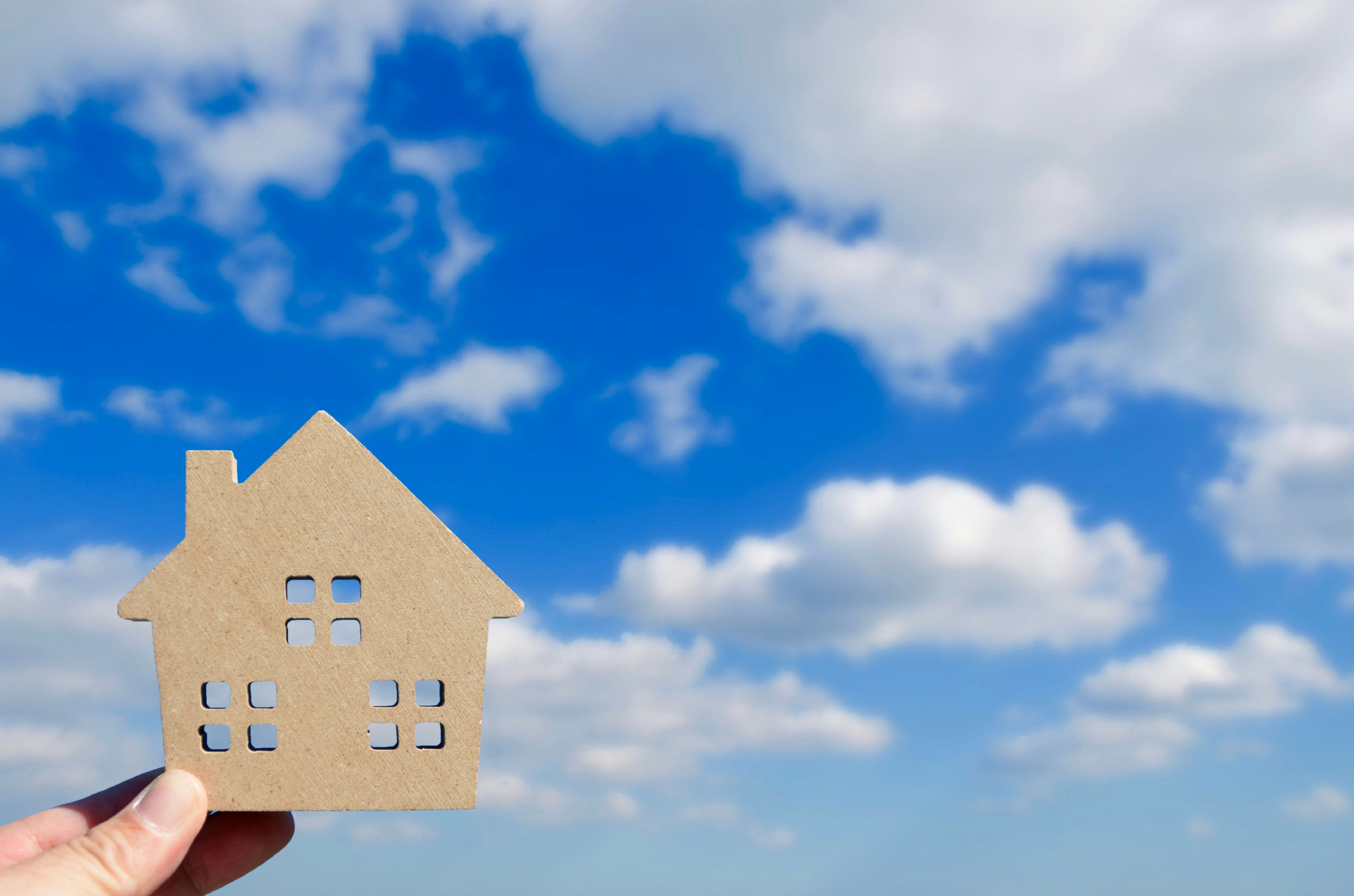 Hand holding a cardboard house shape against a blue sky