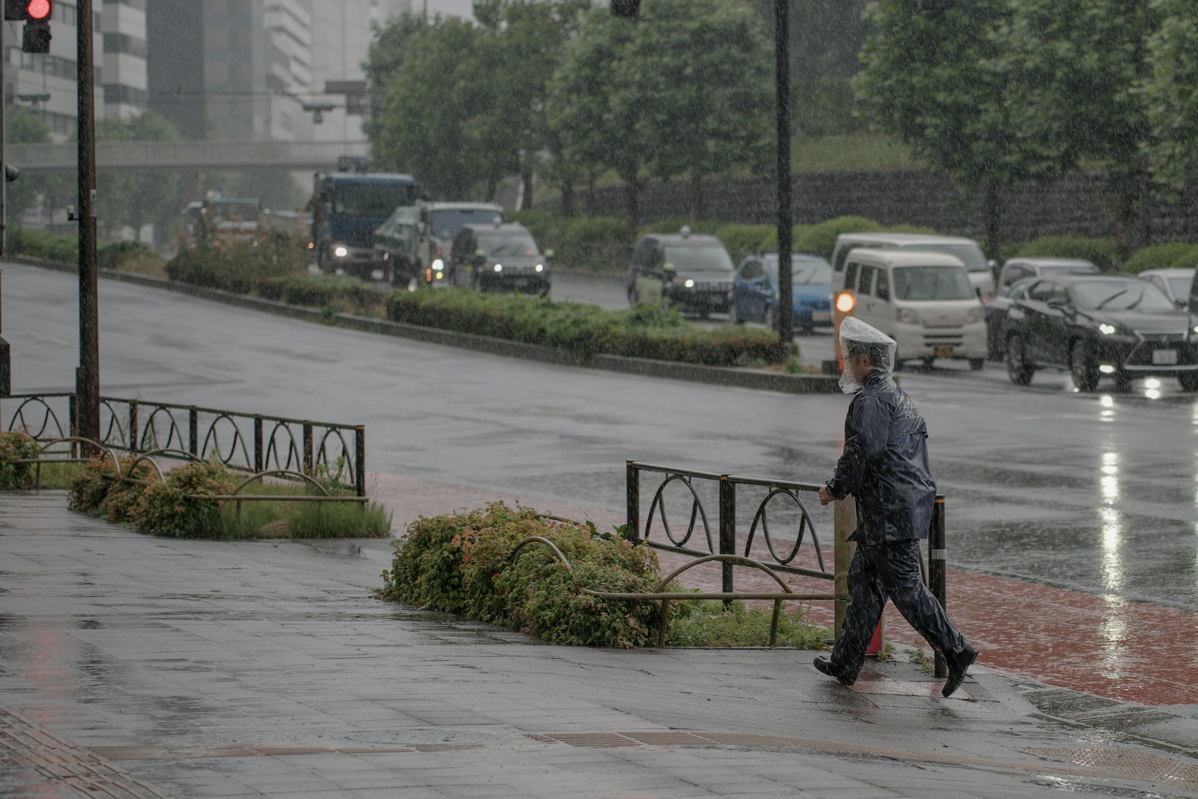 ชายคนหนึ่งเดินอยู่ในสายฝนกับรถที่ผ่านไปในสภาพแวดล้อมในเมือง