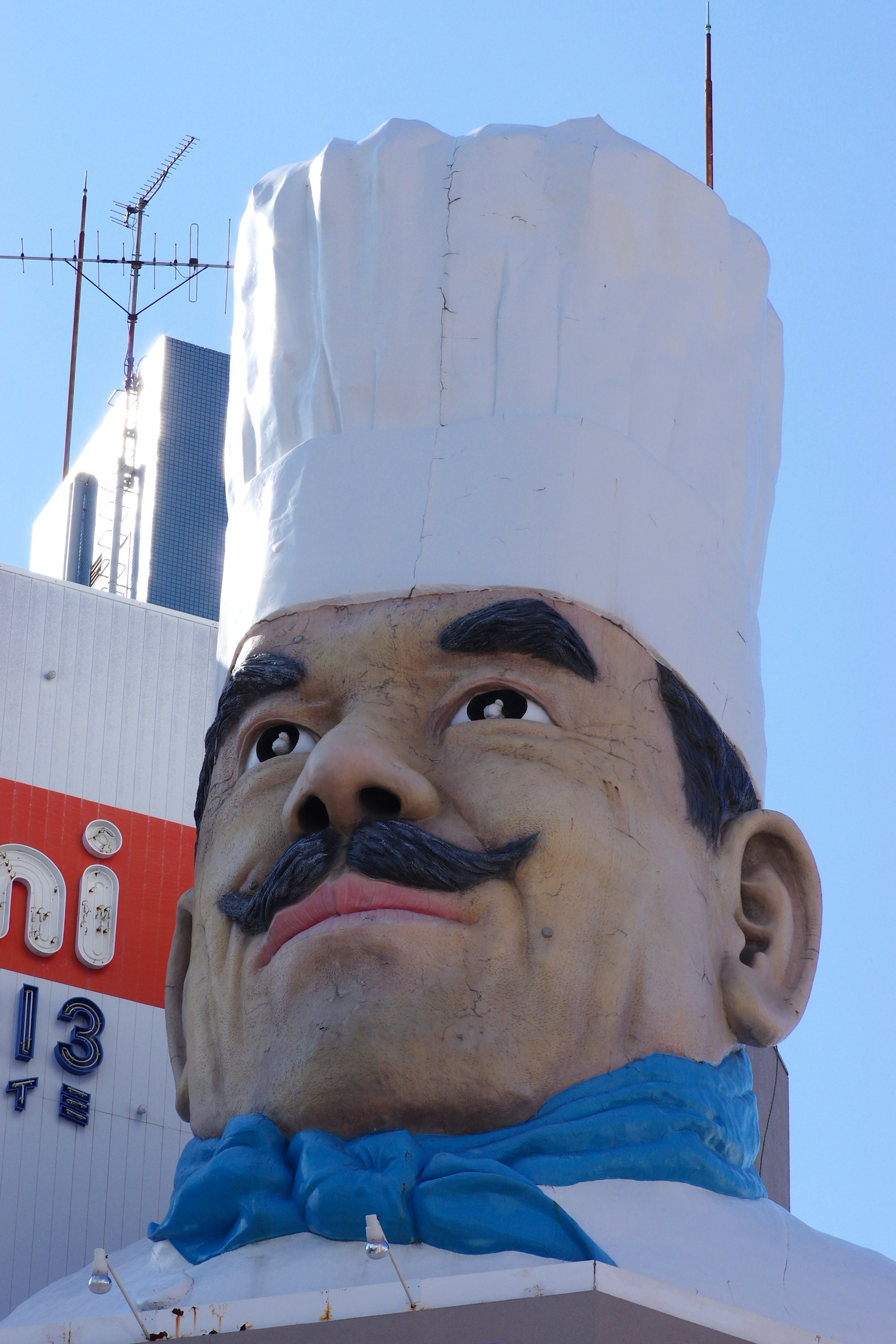 Estatua gigante de chef con gorro blanco y bufanda azul