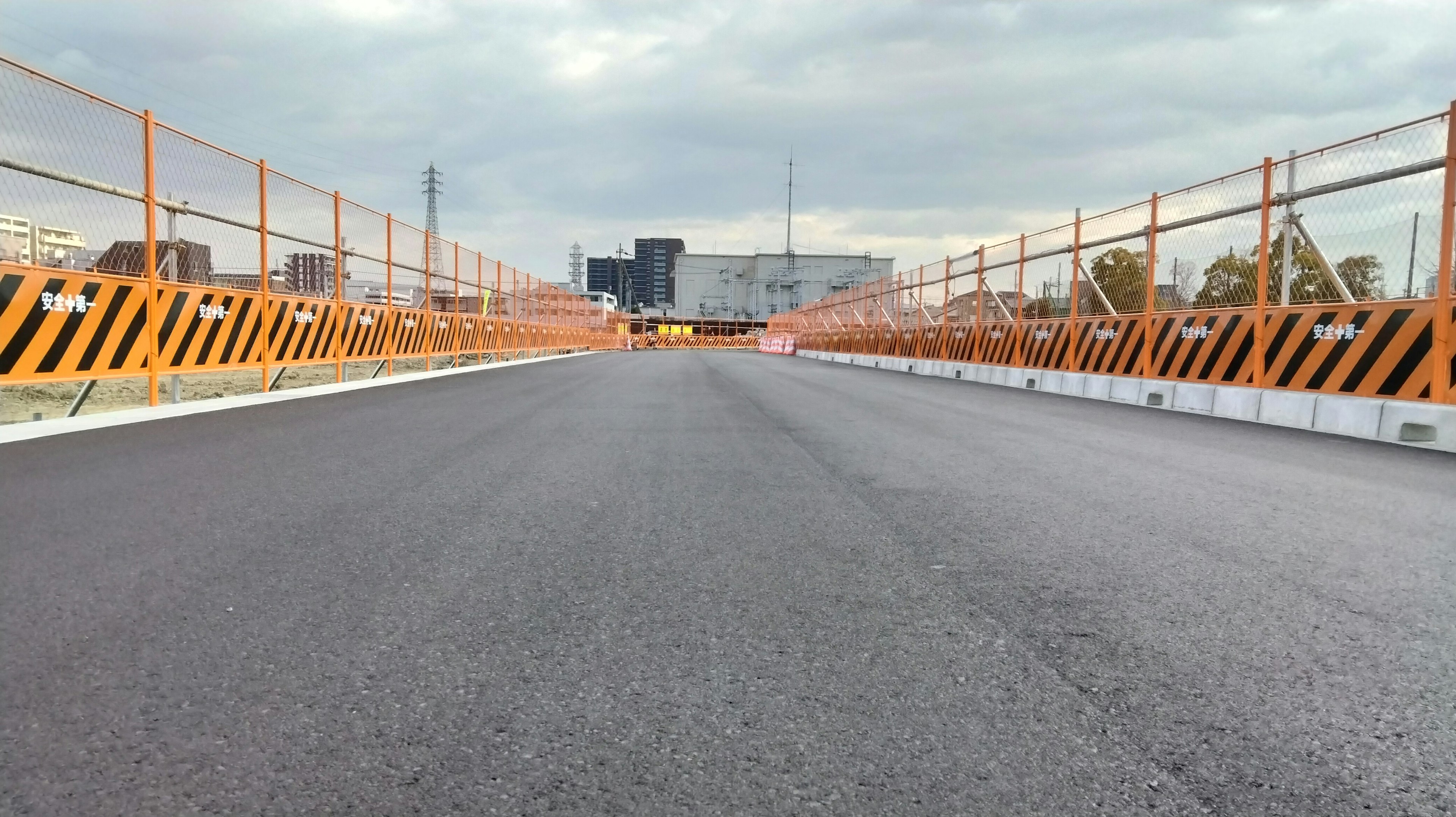 View of a newly paved asphalt road with orange barricades on a bridge