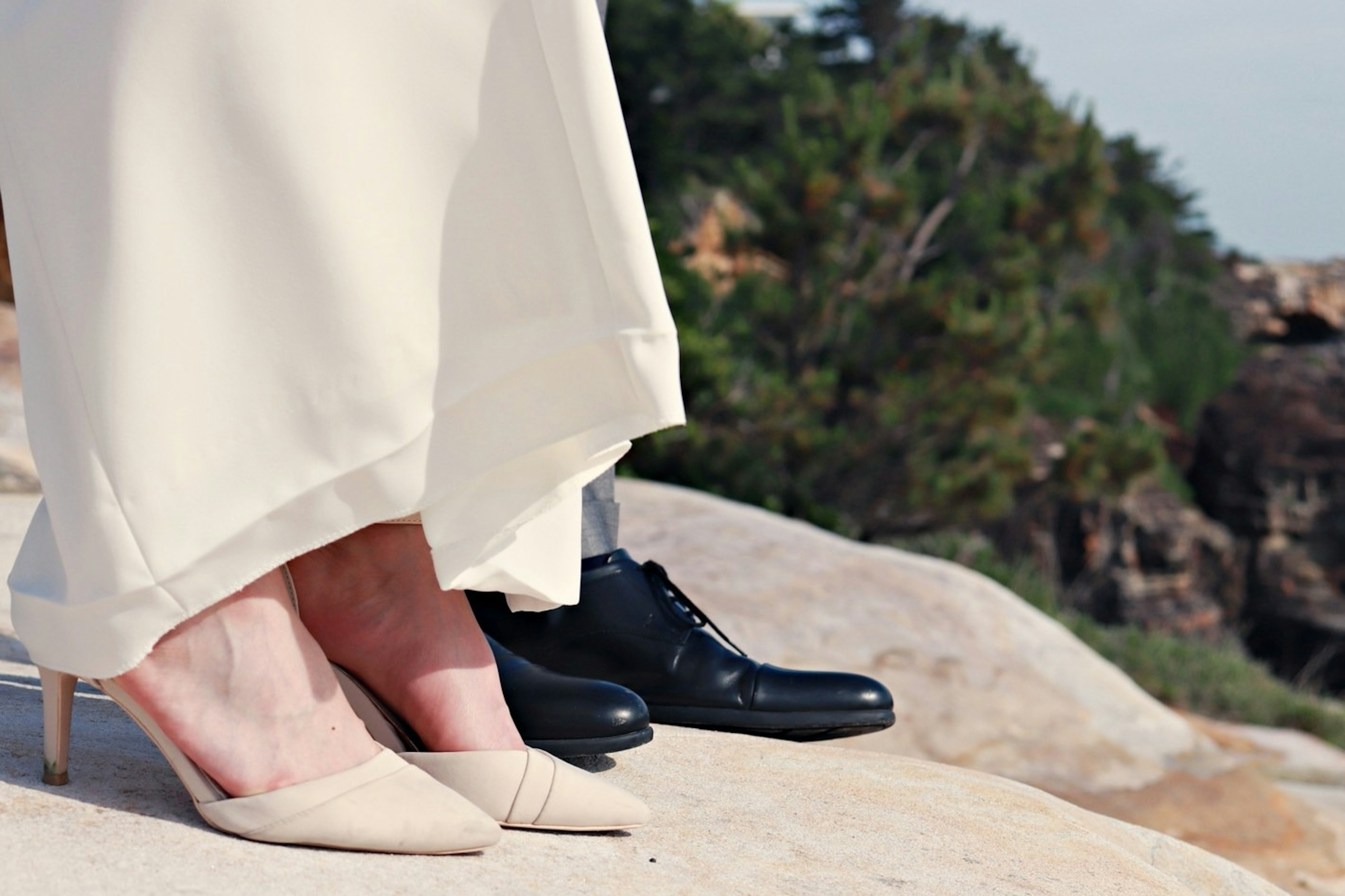 Pies en un vestido blanco y zapatos negros sobre una superficie rocosa