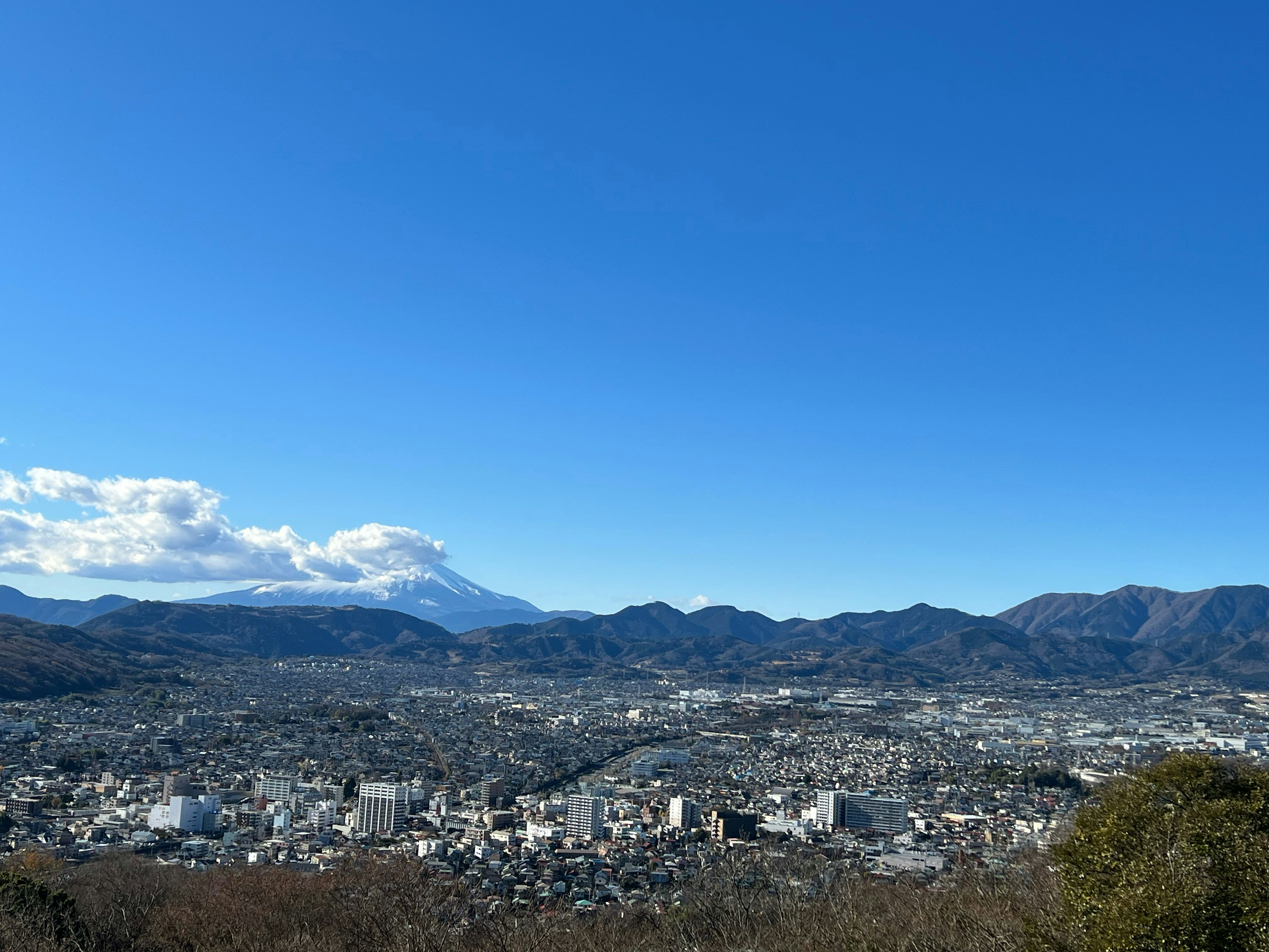 Vista panorámica de una ciudad con el monte Fuji al fondo cielo azul y montañas