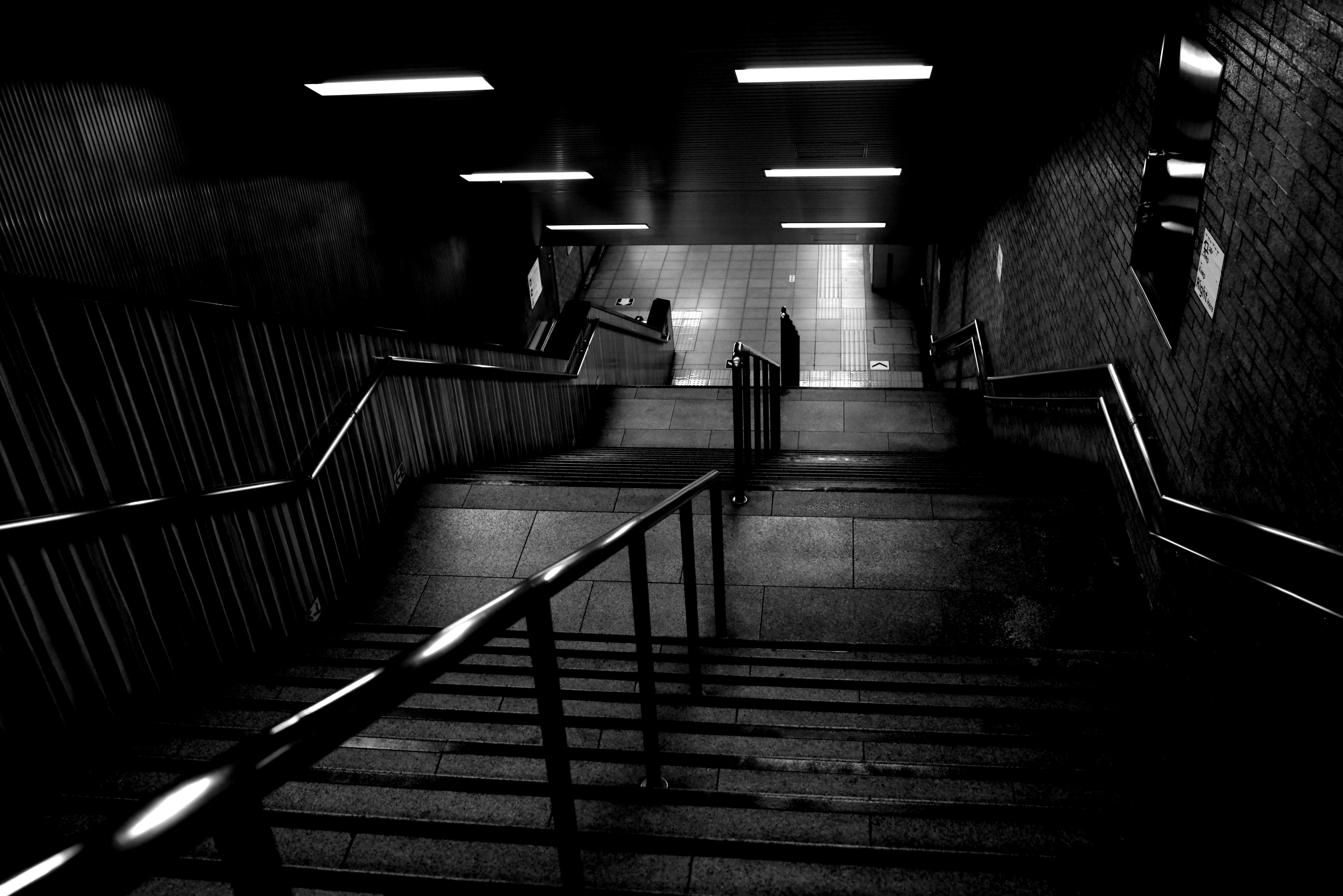 Schwarzweißfoto einer dunklen Treppe, die nach unten führt, mit schwacher Beleuchtung