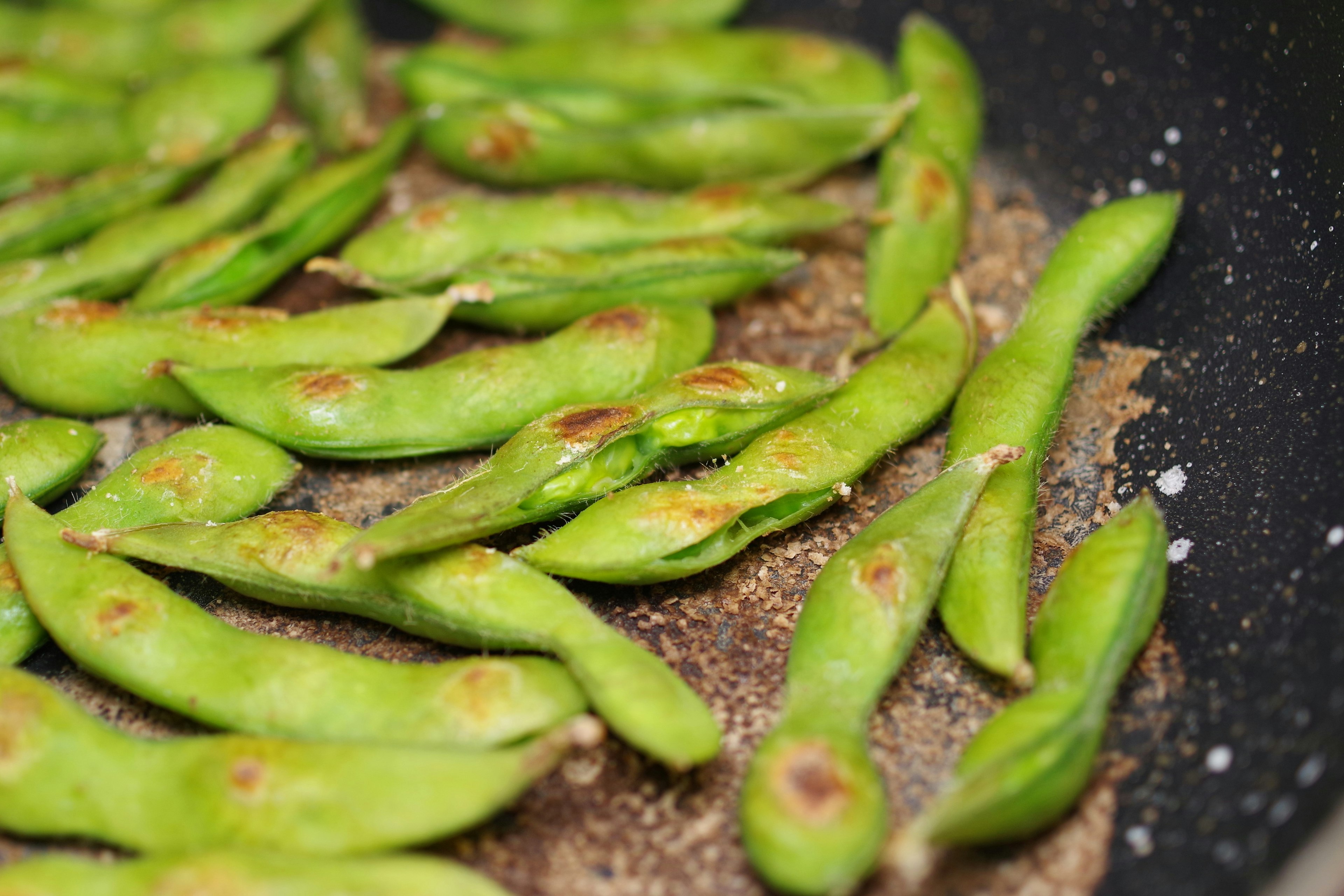 Roasted green edamame pods arranged in a frying pan