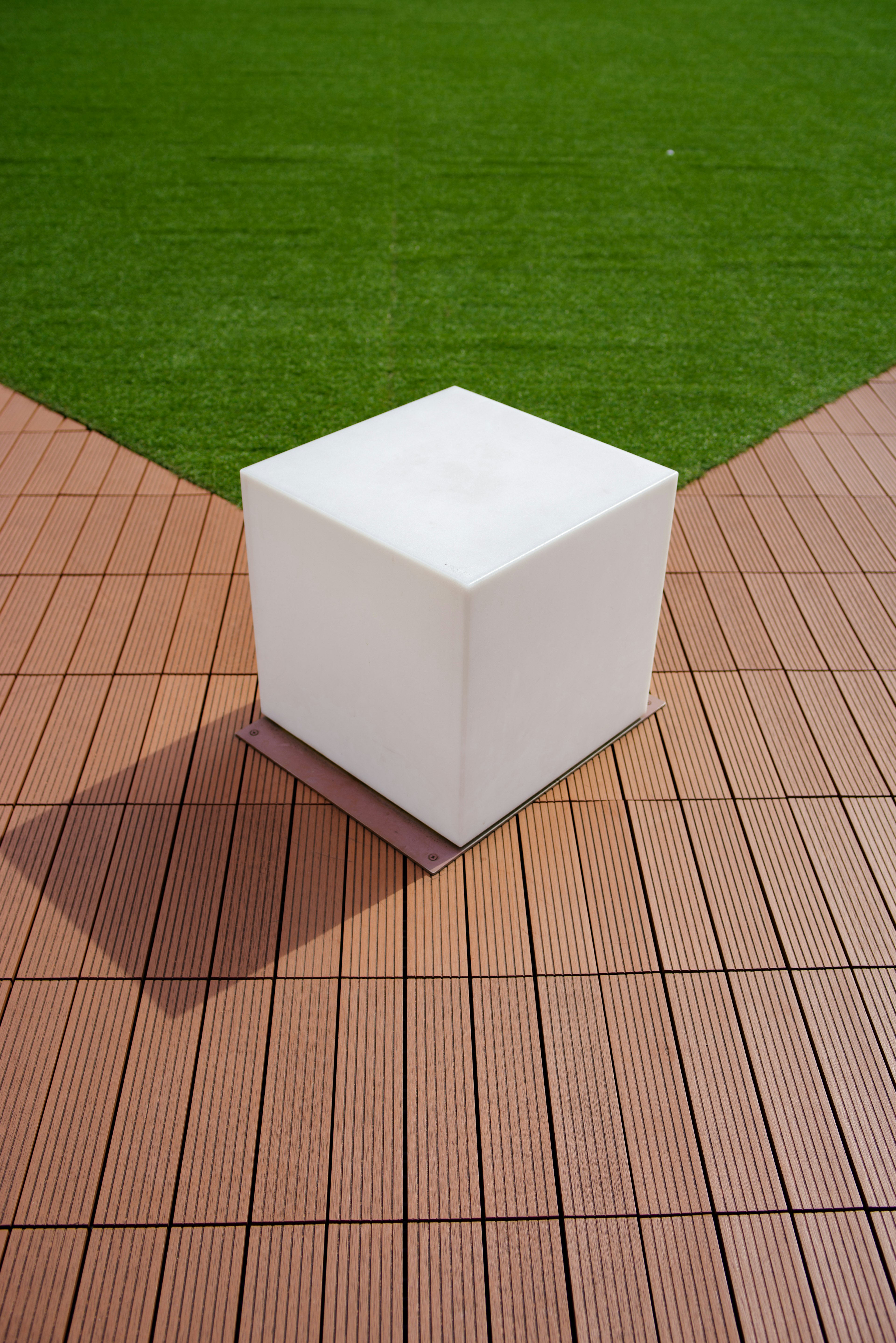 Cubo blanco sobre losas de madera con fondo de césped verde