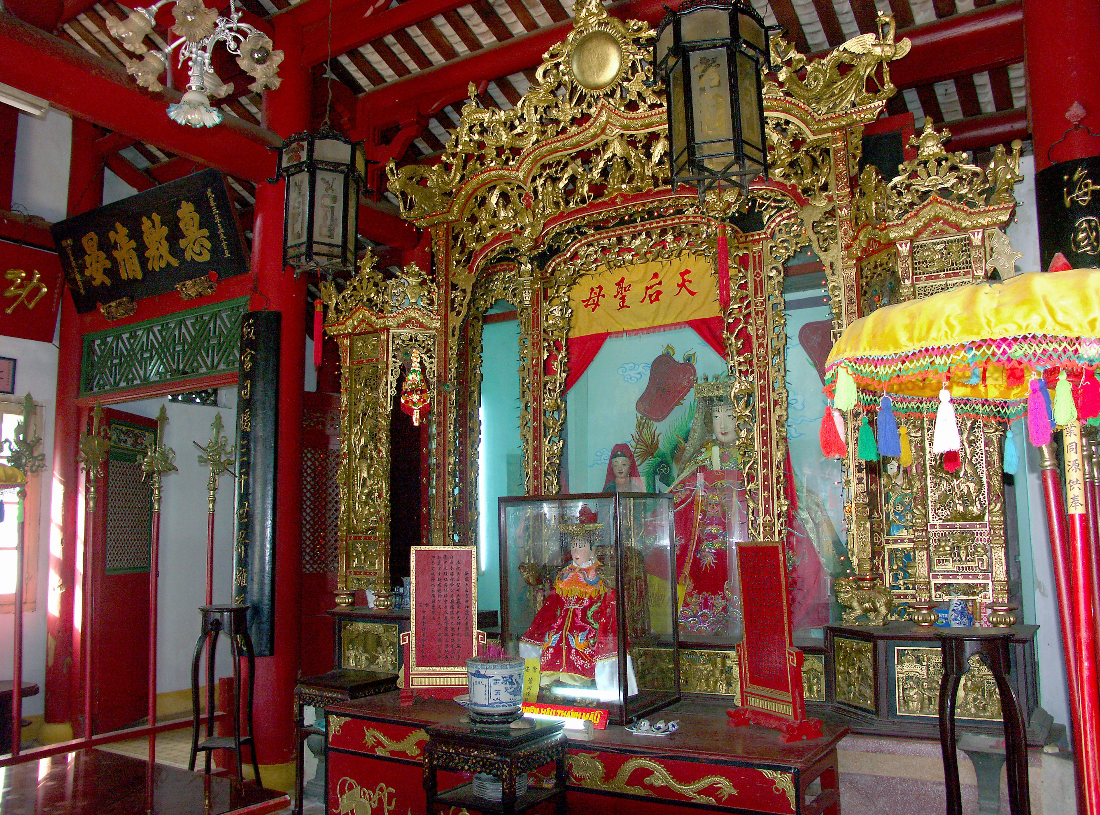 Interior de un templo con decoraciones rojas y doradas, un altar y una estatua que muestran elementos de la cultura china tradicional