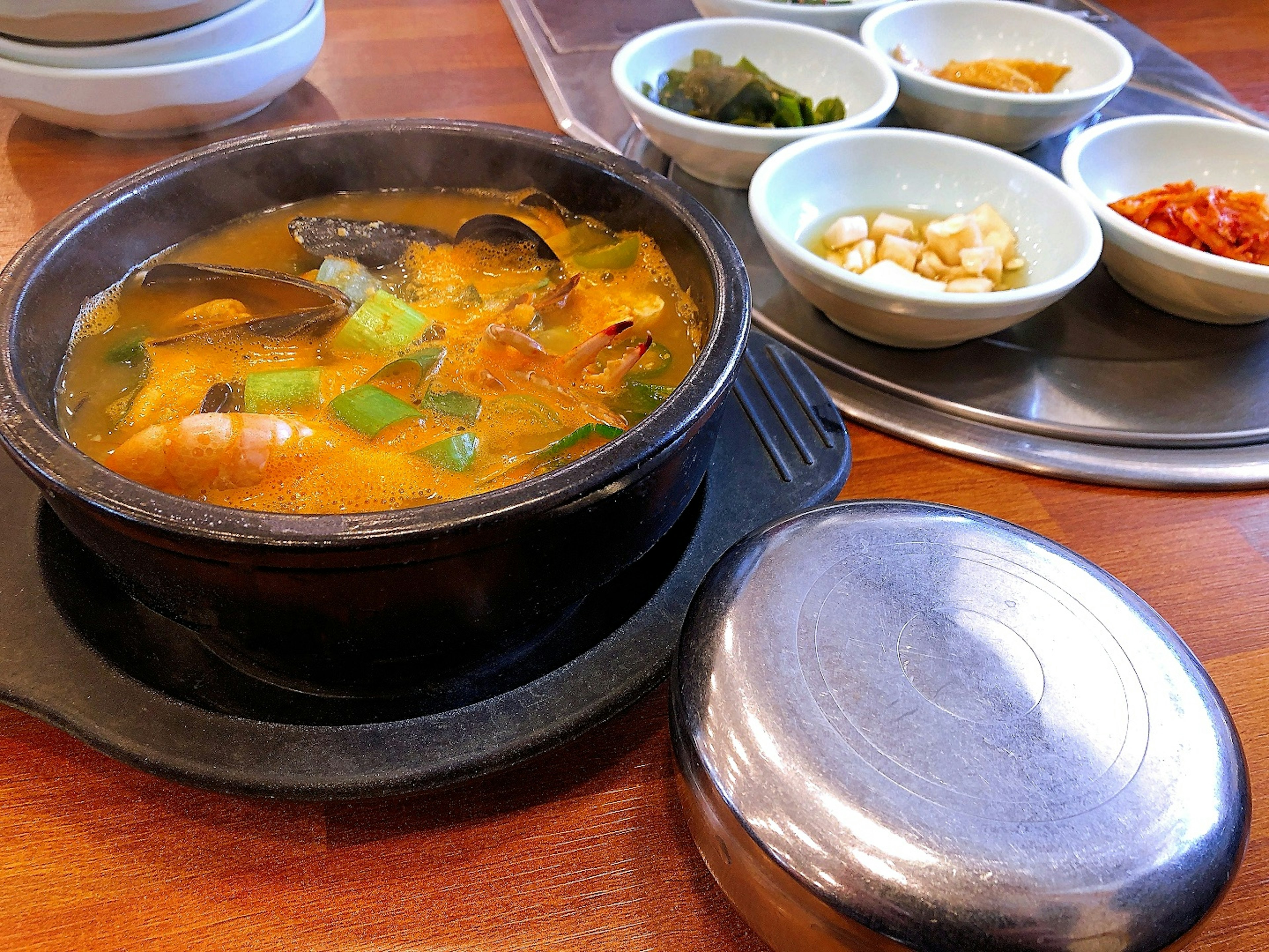 Black pot of seafood soup with side dishes in small bowls