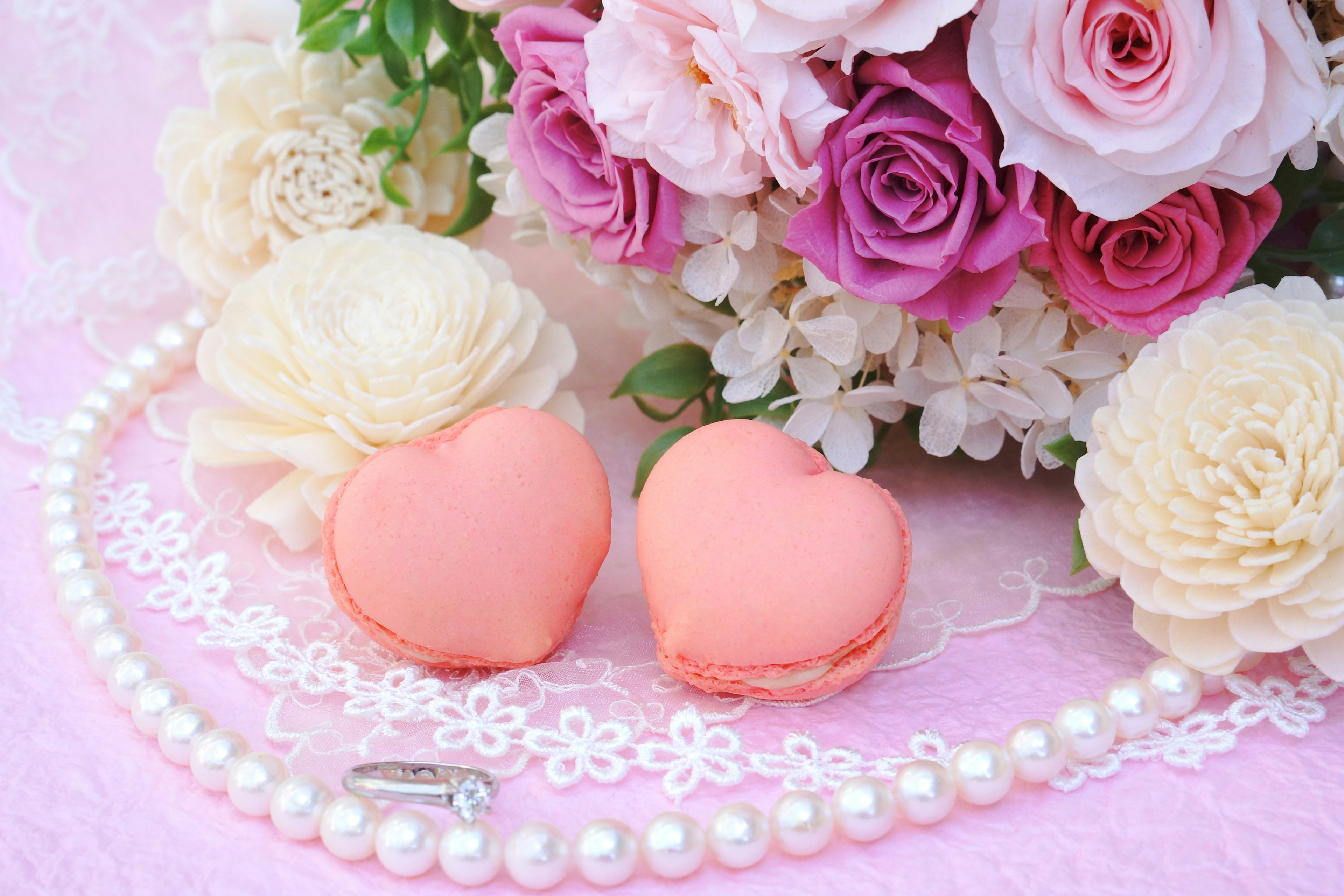 Macarons en forma de corazón junto a un arreglo floral sobre un fondo rosa