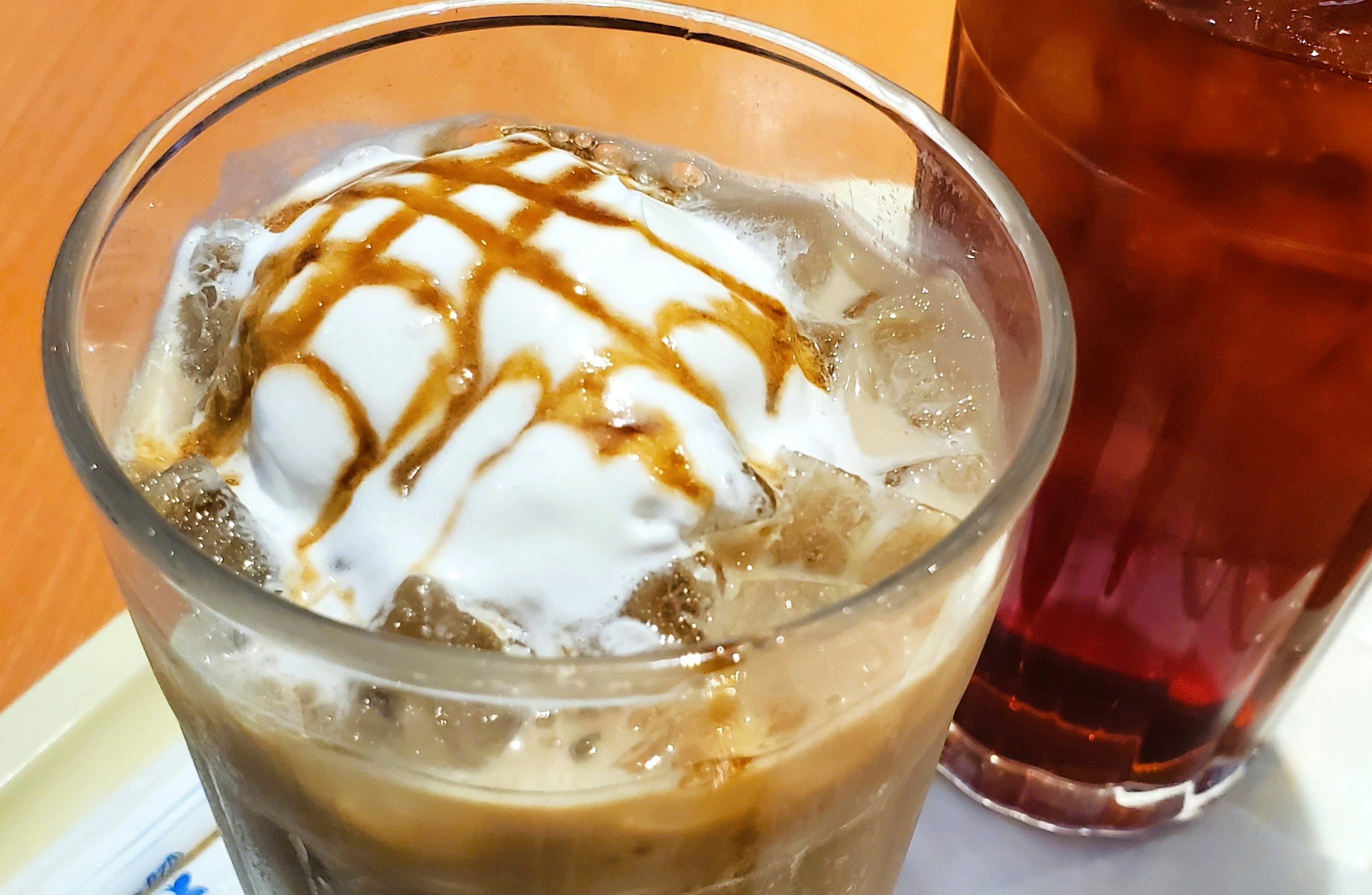 Café helado con crema batida y salsa de caramelo junto a té helado