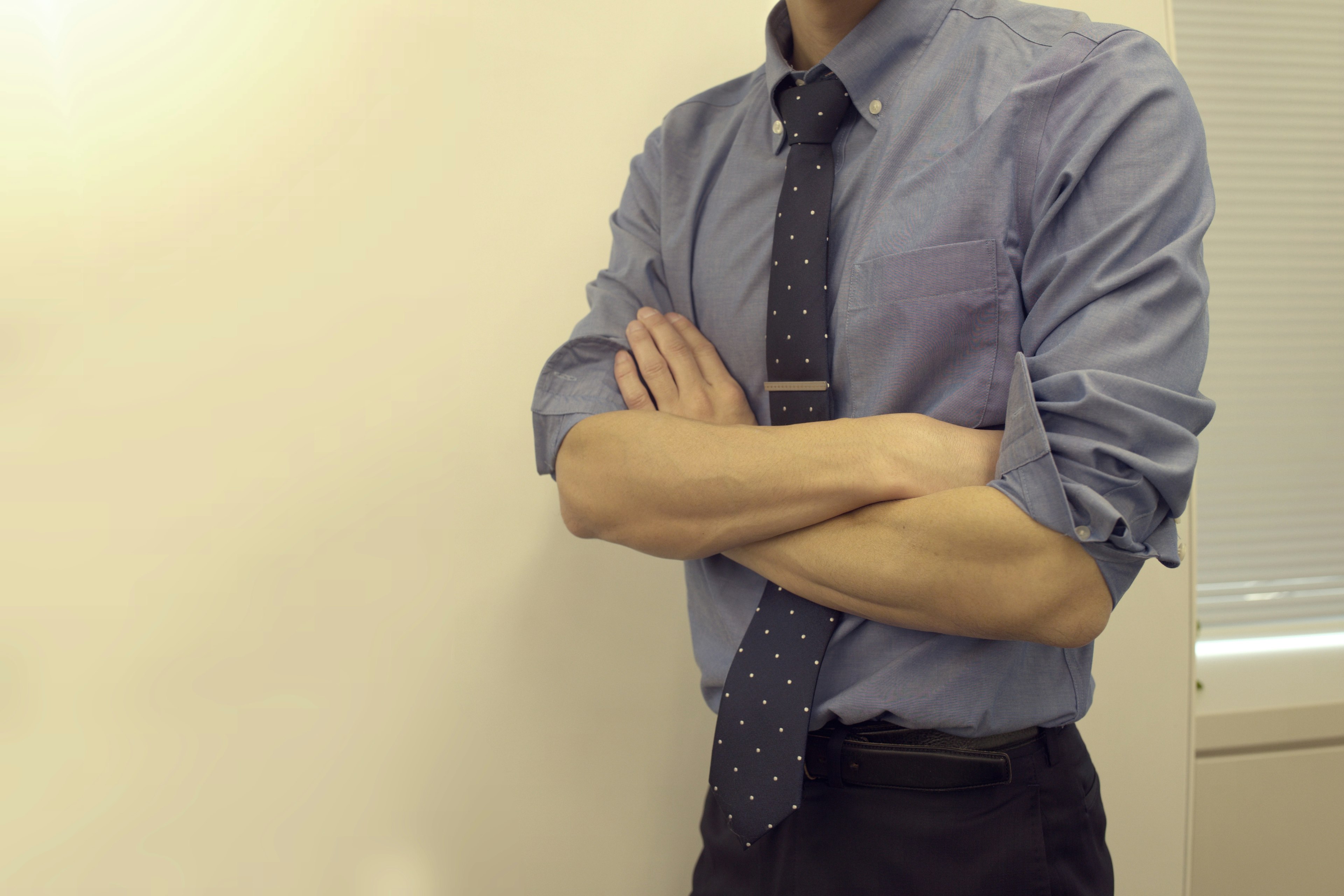 A man in a shirt and tie standing with crossed arms