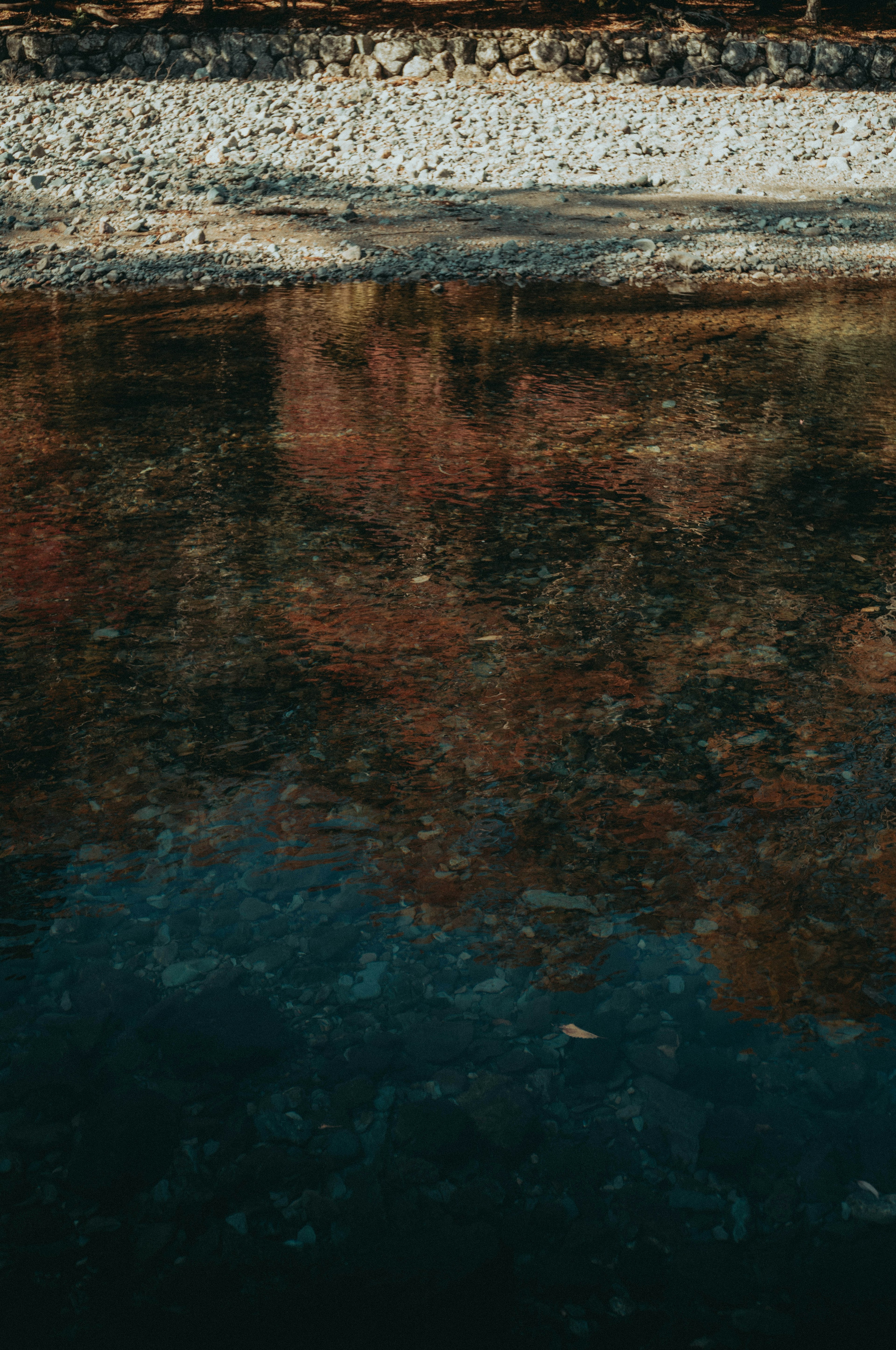 Follaje de otoño reflejado en la superficie del agua con una orilla rocosa