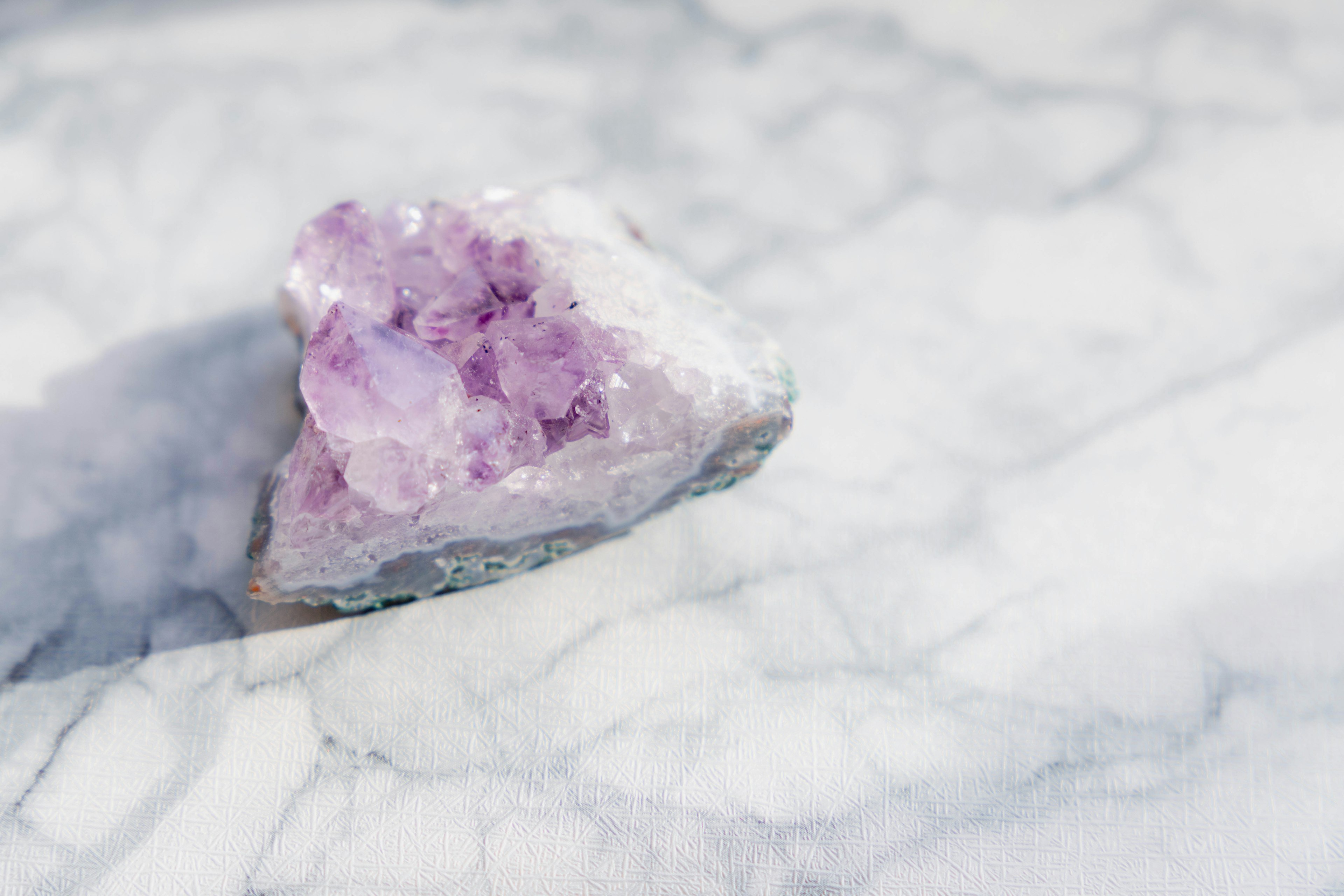 Amethyst crystal with purple hues resting on white marble surface